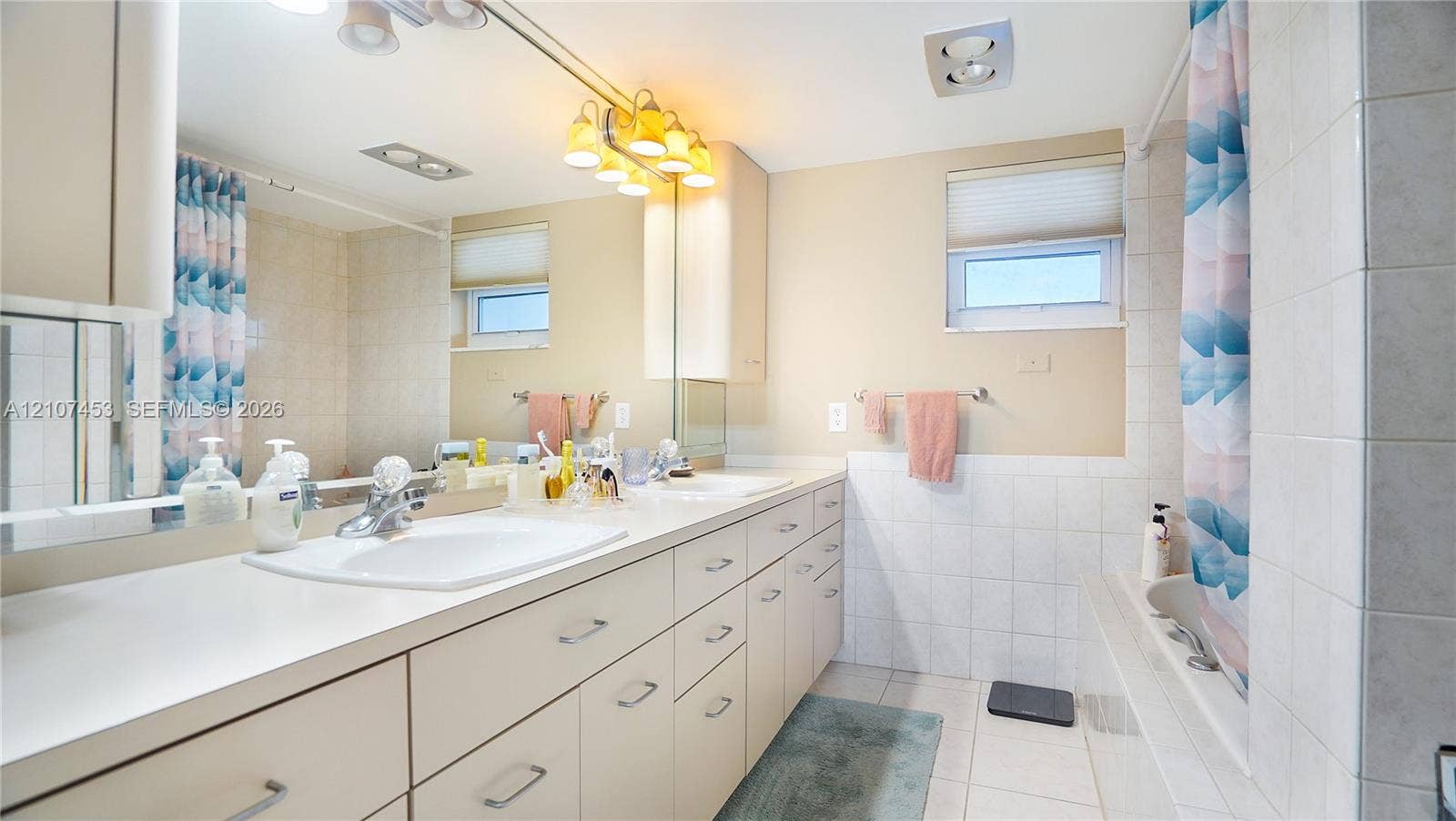 111 N Pompano Beach Boulevard, #304, Pompano Beach, FL 33062 Bathroom featuring a full-width vanity with dual integrated sinks, extensive cabinetry, a large wall-mounted mirror, and tile-surround tub
