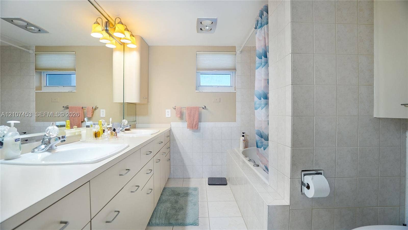 111 N Pompano Beach Boulevard, #304, Pompano Beach, FL 33062 Full-width vanity with integrated dual sinks, expansive wall-to-wall mirror, built-in medicine cabinet, and a tiled bathtub surround
