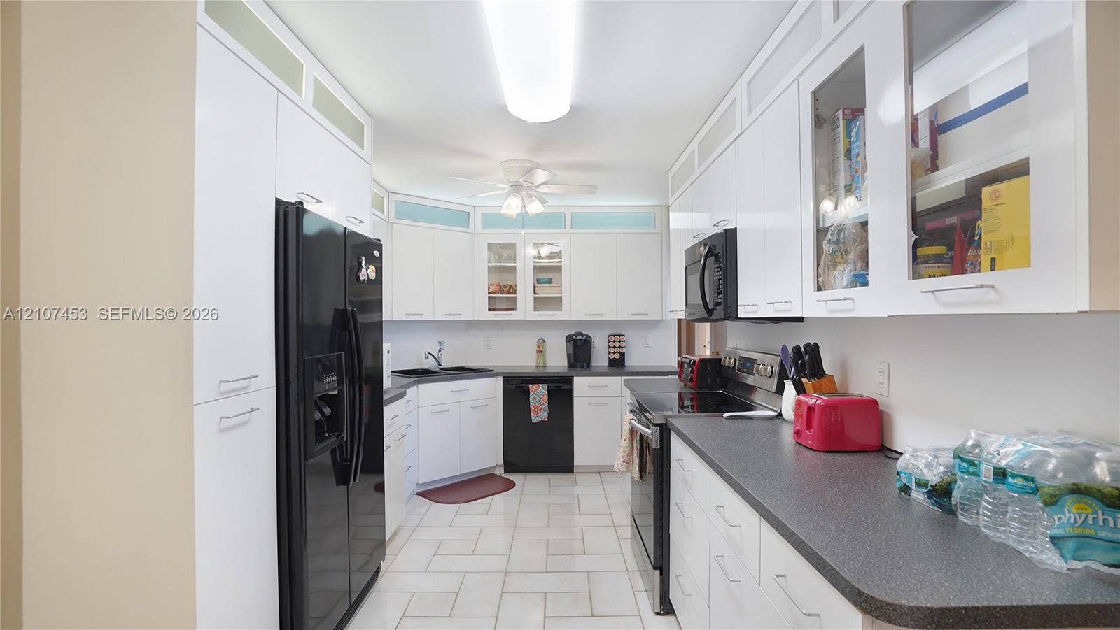 111 N Pompano Beach Boulevard, #304, Pompano Beach, FL 33062 Kitchen featuring white cabinetry with glass-panel upper doors, dark stone-finish countertops, tile flooring, and integrated black appliances