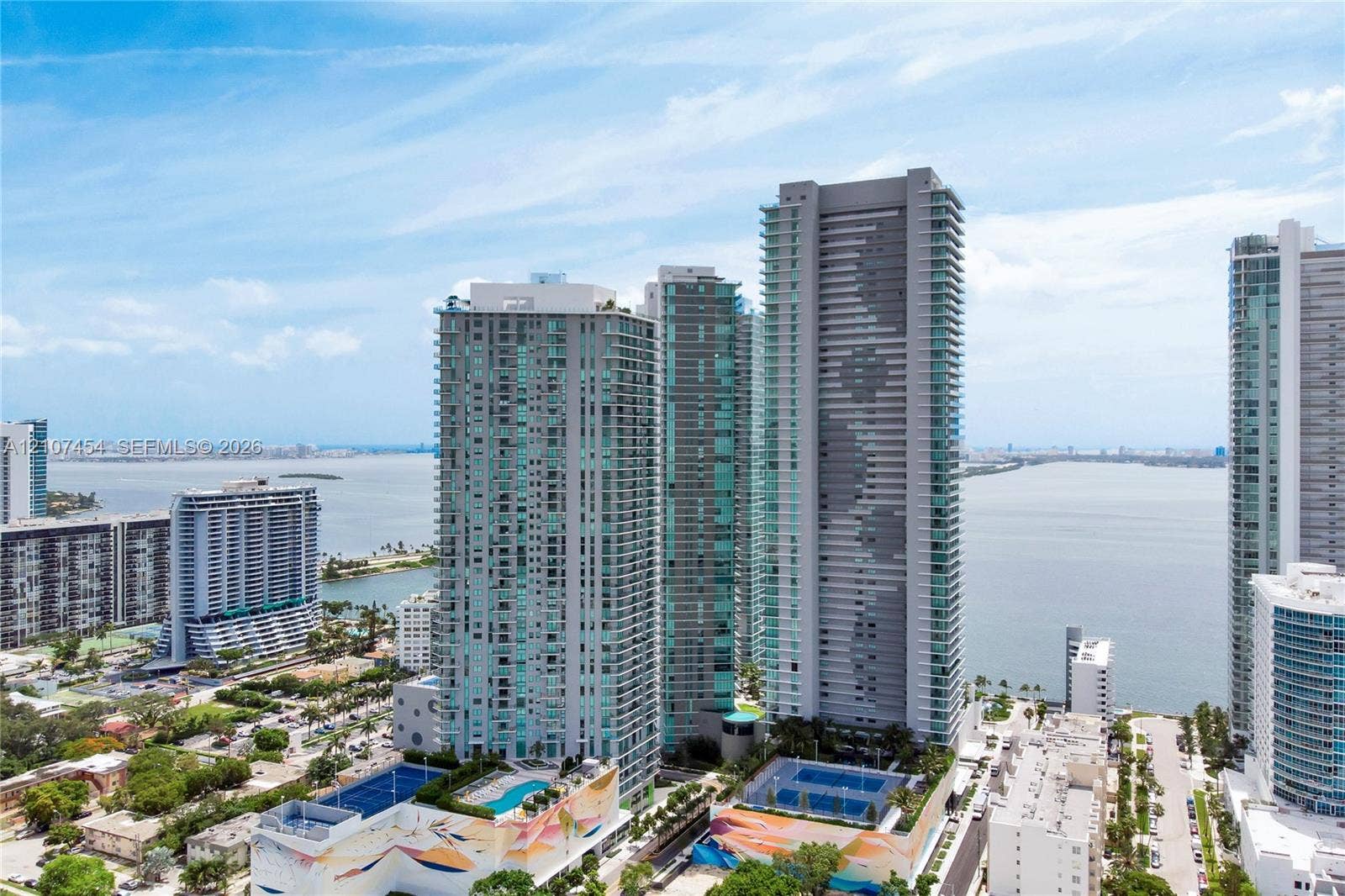 501 NE 31st Street, #1906, Miami, FL 33137 Aerial perspective of a high-rise residential complex featuring glass-facade towers, outdoor swimming pools, and tennis courts situated along the waterfront