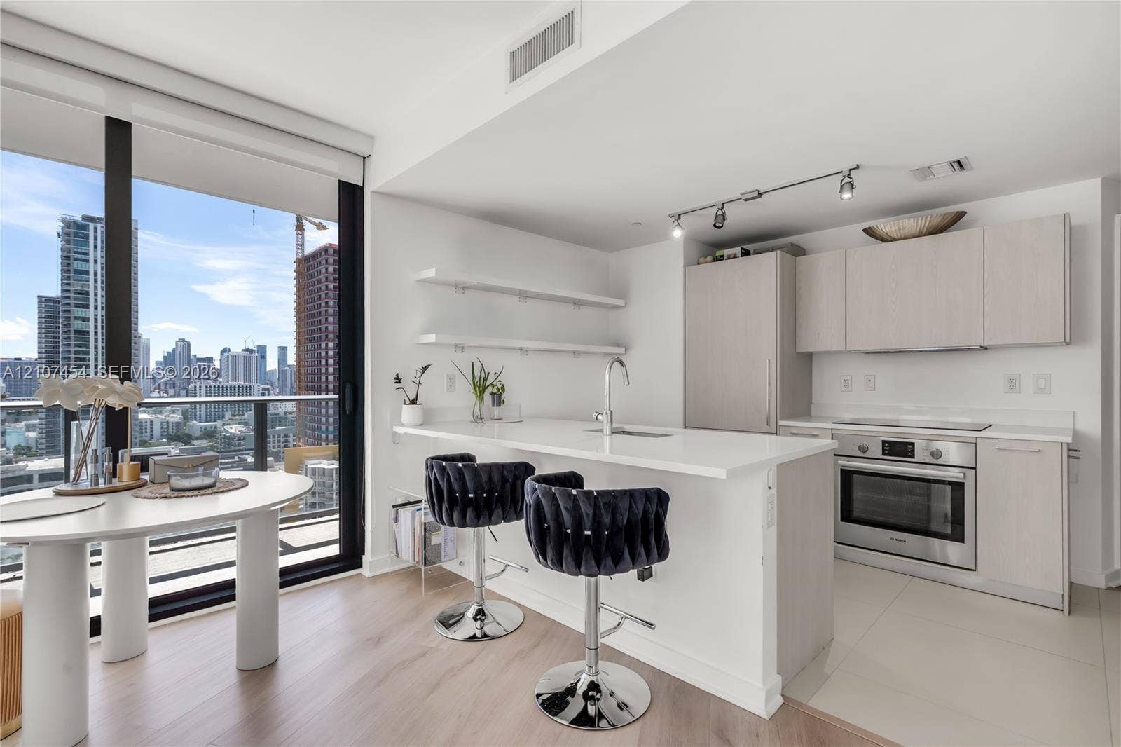 501 NE 31st Street, #1906, Miami, FL 33137 Kitchen featuring a quartz-topped island, light wood-finish cabinetry, built-in stainless steel oven, floor-to-ceiling windows, and floating shelving