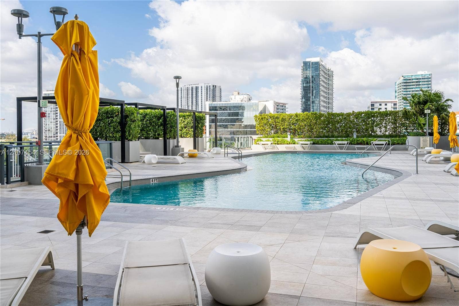 501 NE 31st Street, #1906, Miami, FL 33137 Rooftop pool featuring light-toned tile decking, integrated metal pergolas, manicured hedge privacy screening, and stainless steel pool railings