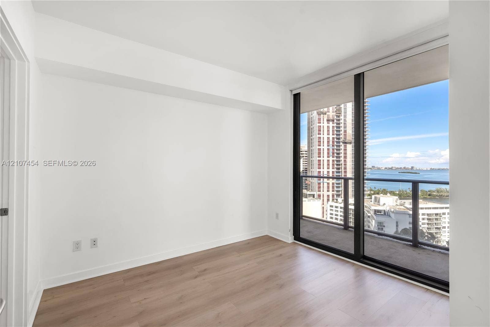 501 NE 31st Street, #1906, Miami, FL 33137 Interior room featuring wood-finish flooring, floor-to-ceiling windows, and access to a private balcony with water and city skyline surroundings
