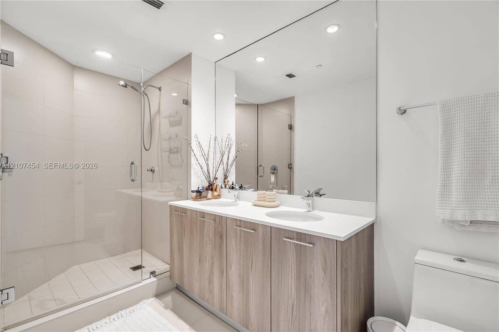 501 NE 31st Street, #1906, Miami, FL 33137 Double vanity featuring wood-finish cabinetry, solid surface countertops, dual undermount sinks, and a frameless glass-enclosed shower with tiled walls