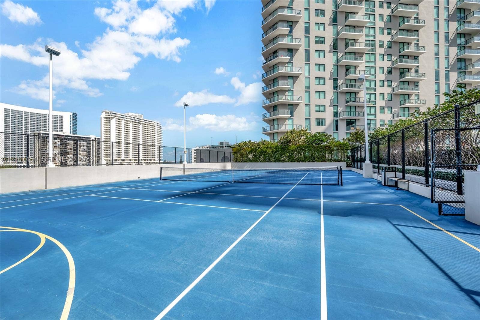 501 NE 31st Street, #1906, Miami, FL 33137 Outdoor tennis court featuring a blue hard-surface finish, perimeter chain-link fencing, court lighting, and painted lines