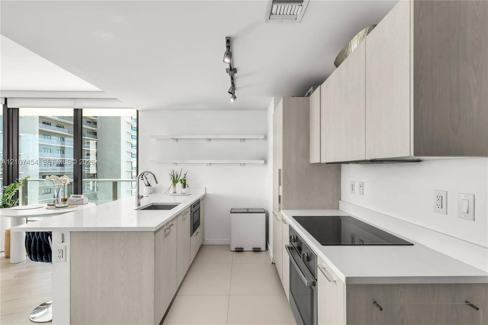 501 NE 31st Street, #1906, Miami, FL 33137 Kitchen featuring light wood-finish cabinetry, white solid-surface countertops, built-in cooktop, undermount stainless steel sink, and wall-mounted track lighting