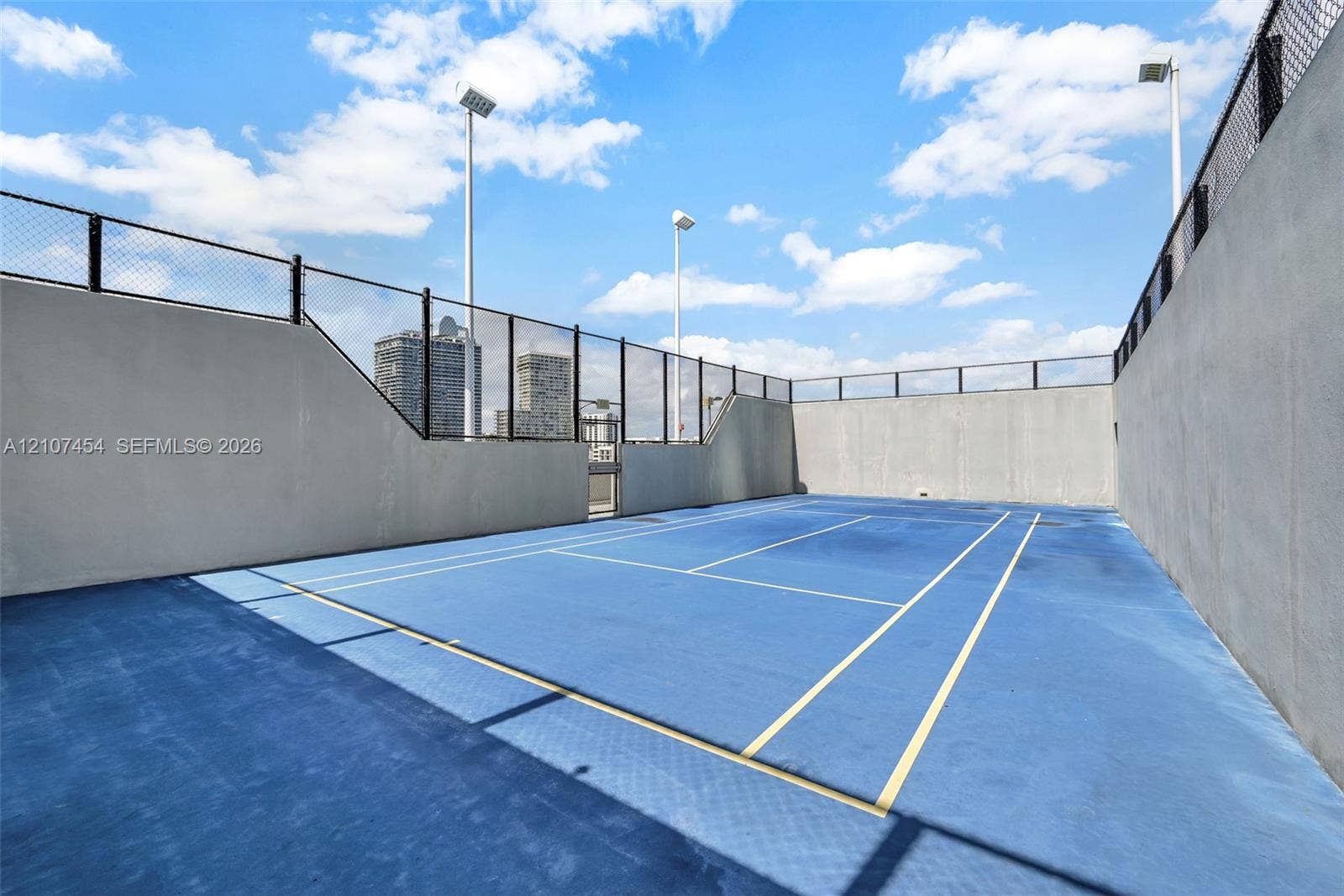 501 NE 31st Street, #1906, Miami, FL 33137 Private tennis court featuring a blue hard-surface finish, perimeter chain-link fencing, and elevated pole lighting