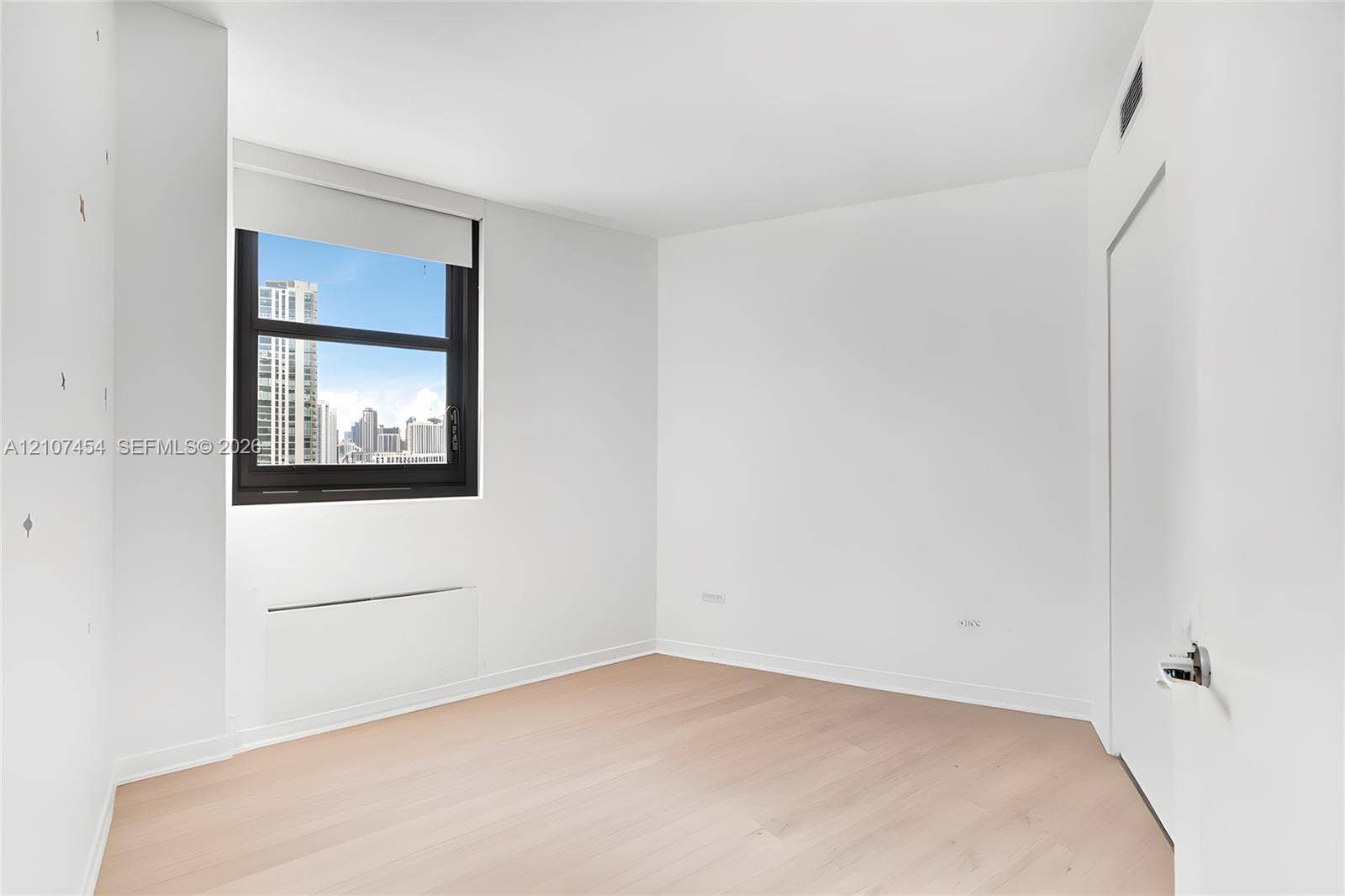 501 NE 31st Street, #1906, Miami, FL 33137 Light-filled interior featuring wood-finish flooring, a large window with urban skyline exposure, and clean, neutral wall finishes