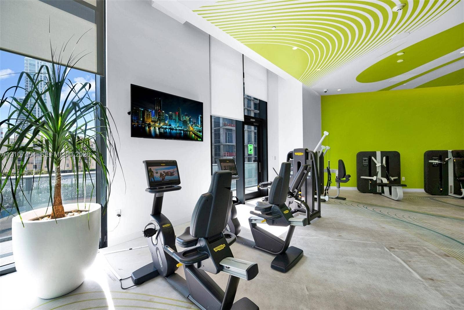 501 NE 31st Street, #1906, Miami, FL 33137 Fitness facility featuring floor-to-ceiling windows, high ceilings with decorative acoustic panels, polished concrete flooring, and wall-mounted television