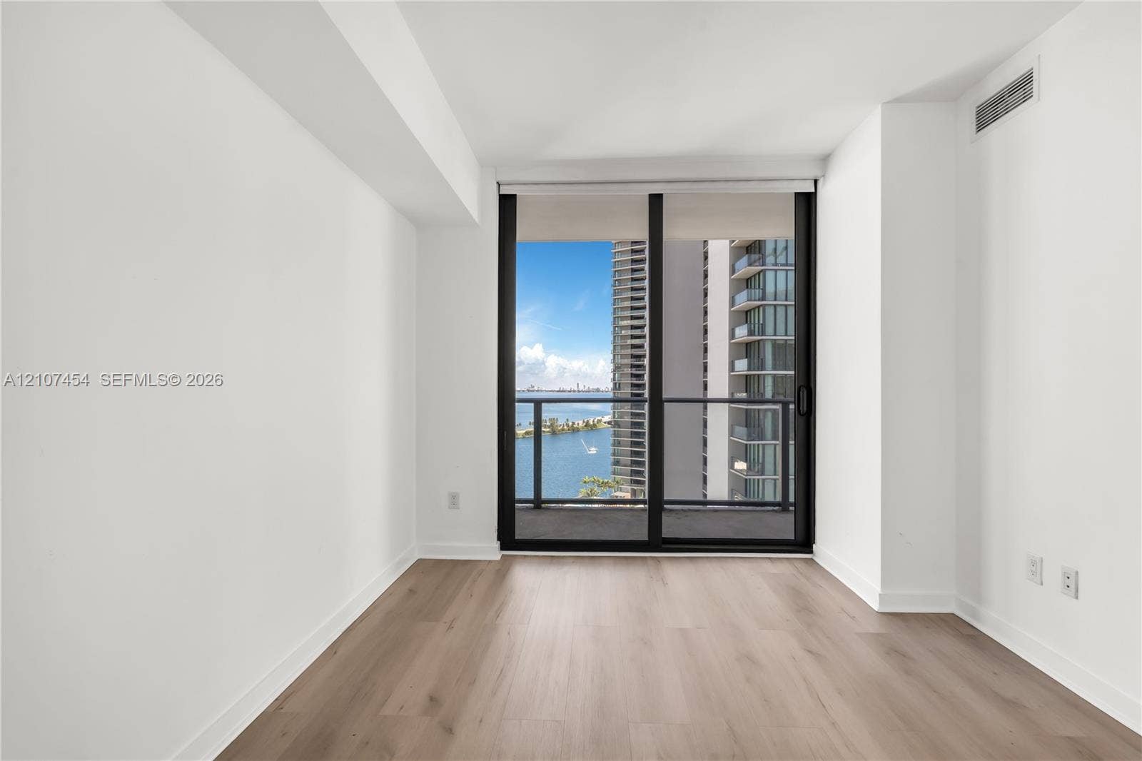 501 NE 31st Street, #1906, Miami, FL 33137 Floor-to-ceiling sliding glass doors opening to a private balcony with water and urban scenery, complemented by light wood-finish flooring