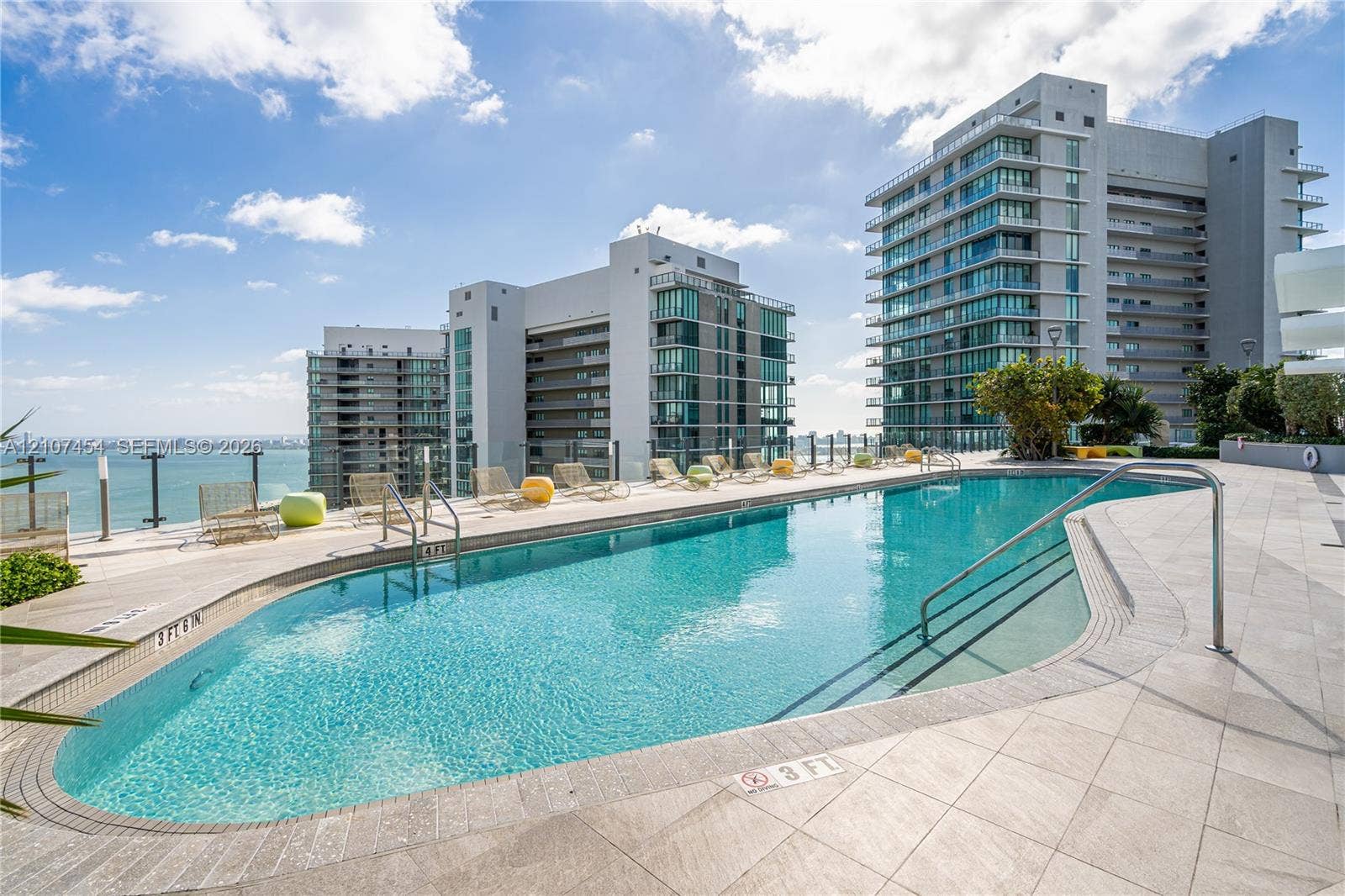 501 NE 31st Street, #1906, Miami, FL 33137 Curved swimming pool featuring a tile surround, metal handrails, and a glass panel perimeter fence