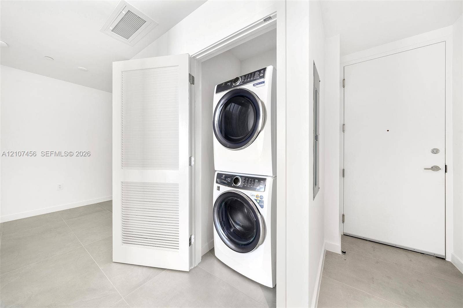1400 Biscayne Boulevard, #2604, Miami, Miami, FL 33132 Stacked front-load laundry unit housed within a dedicated closet featuring louvered doors and large-format neutral floor tile