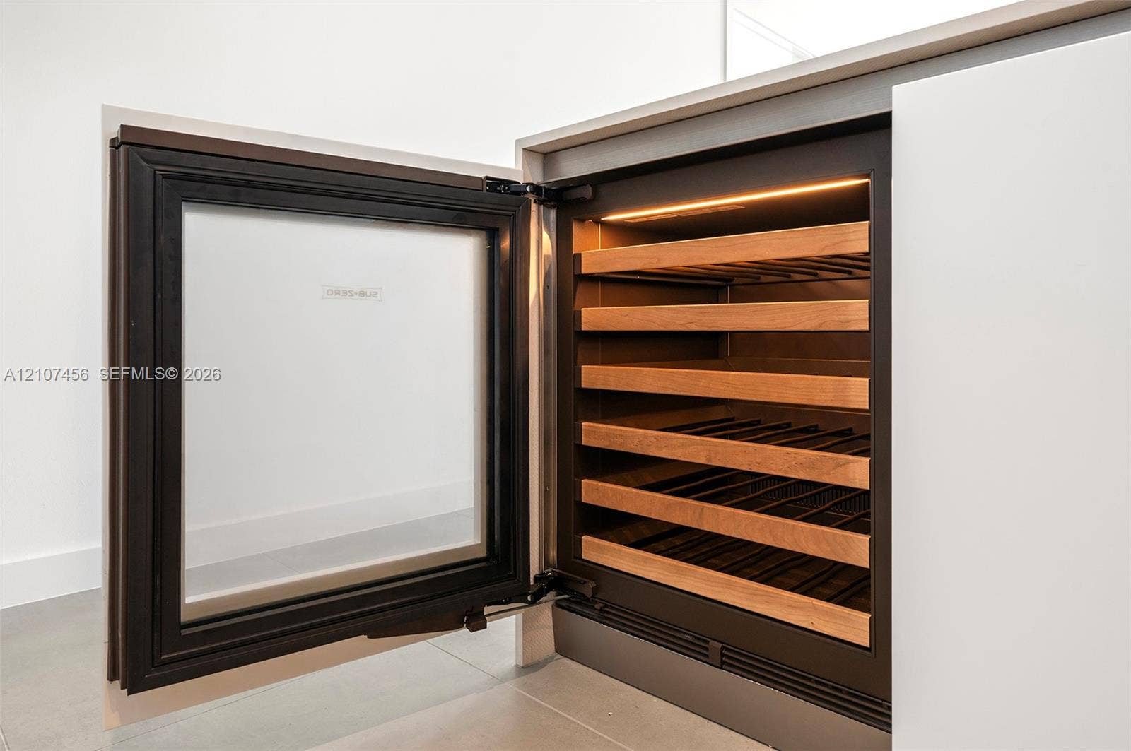 1400 Biscayne Boulevard, #2604, Miami, Miami, FL 33132 Built-in under-counter beverage refrigerator featuring a glass door, matte black frame, integrated internal lighting, and horizontal wood-finish shelving