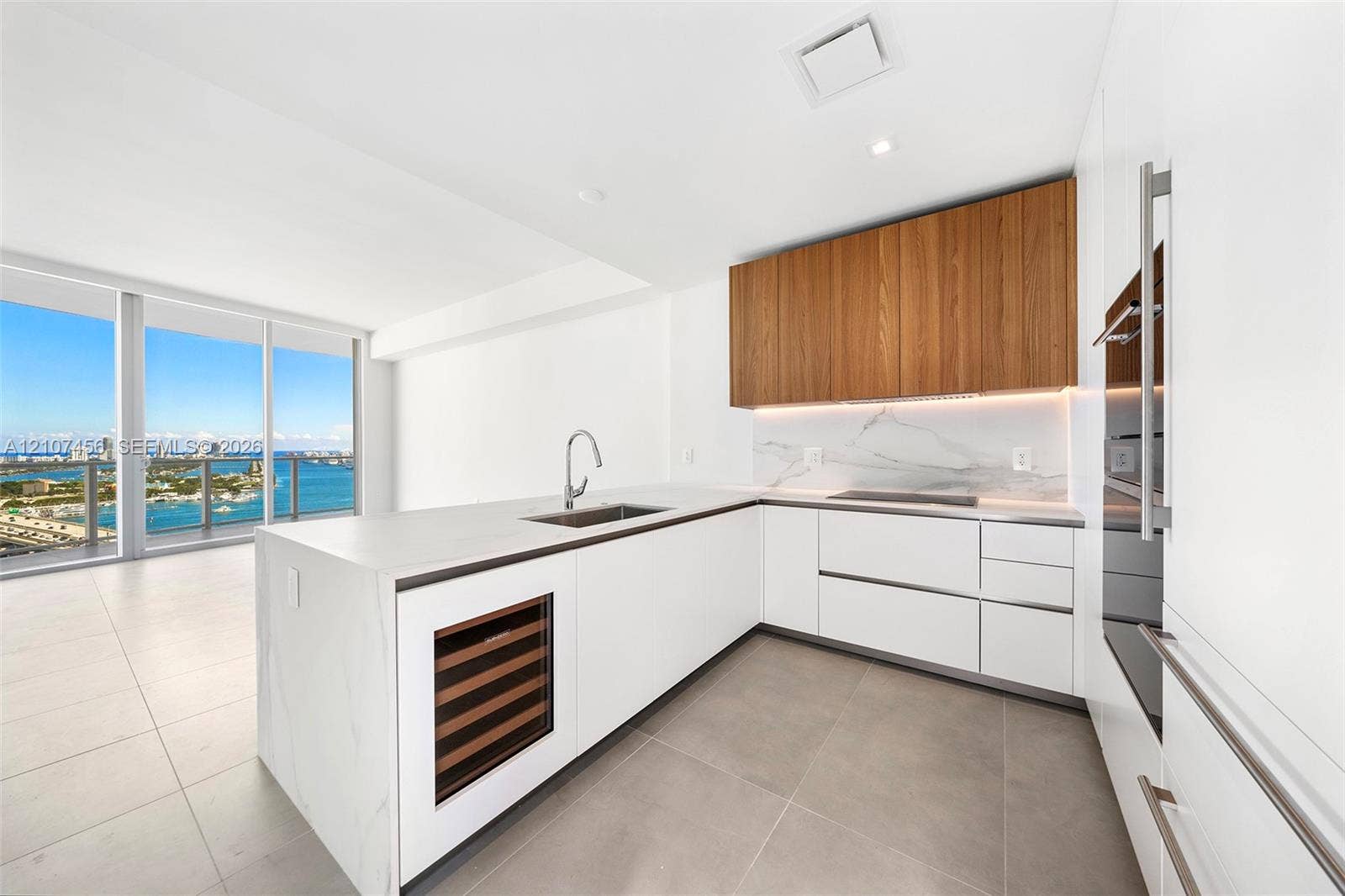 1400 Biscayne Boulevard, #2604, Miami, Miami, FL 33132 Kitchen featuring flat-panel white cabinetry, wood-finish upper cabinets, stone-surfaced island with integrated wine refrigeration, under-cabinet lighting, and floor-to-ceiling windows