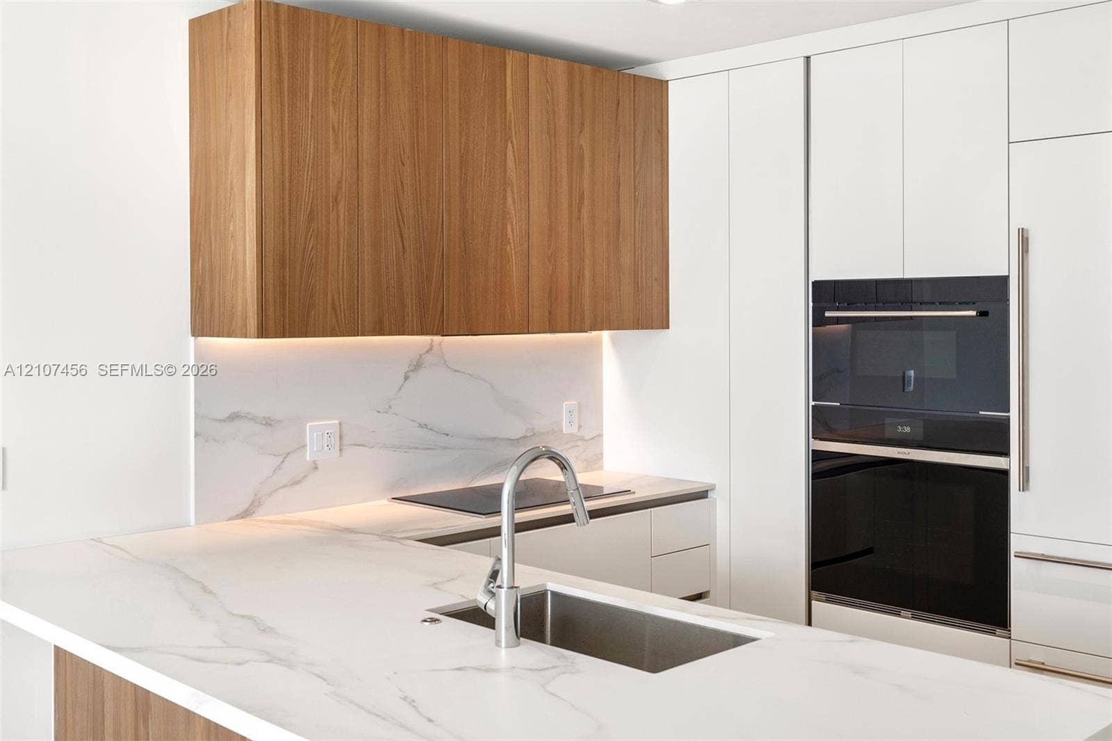 1400 Biscayne Boulevard, #2604, Miami, Miami, FL 33132 Kitchen featuring wood-finish cabinetry, white stone-patterned countertops, integrated stainless steel appliances, and a polished metal gooseneck faucet