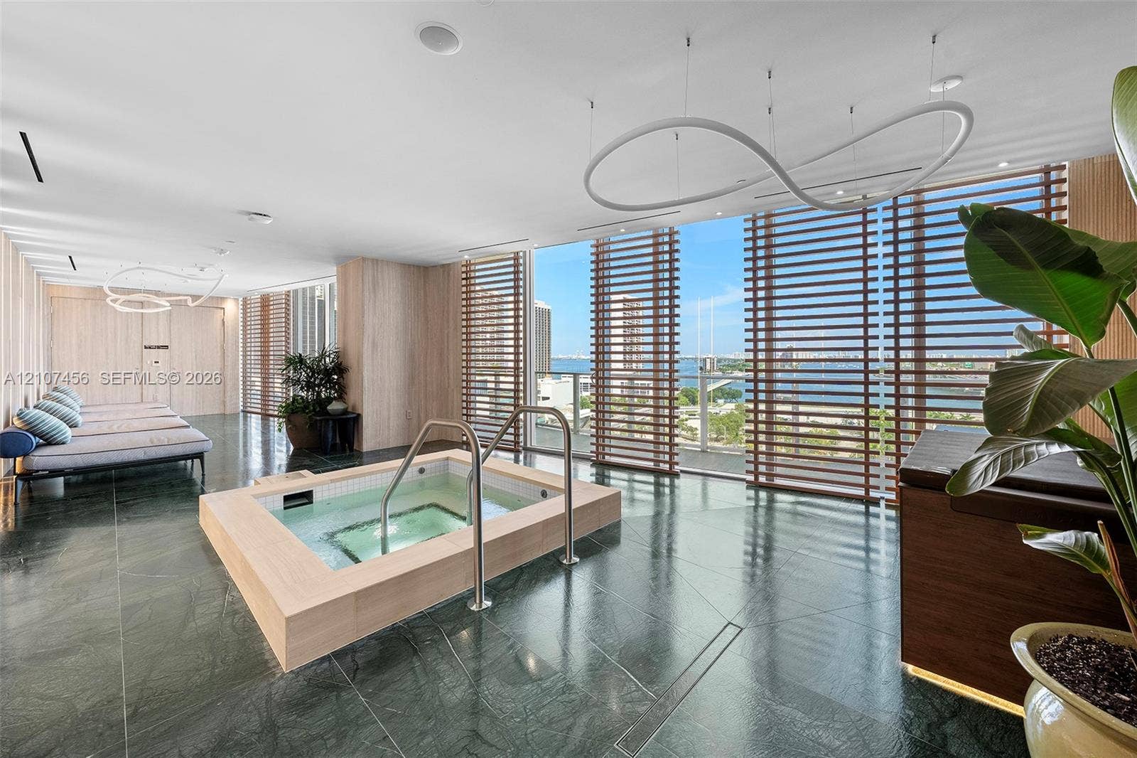 1400 Biscayne Boulevard, #2604, Miami, Miami, FL 33132 Soaking tub with light-wood finish surround, dark stone flooring, floor-to-ceiling windows with horizontal wood-slat privacy screens, and sculptural modern pendant lighting