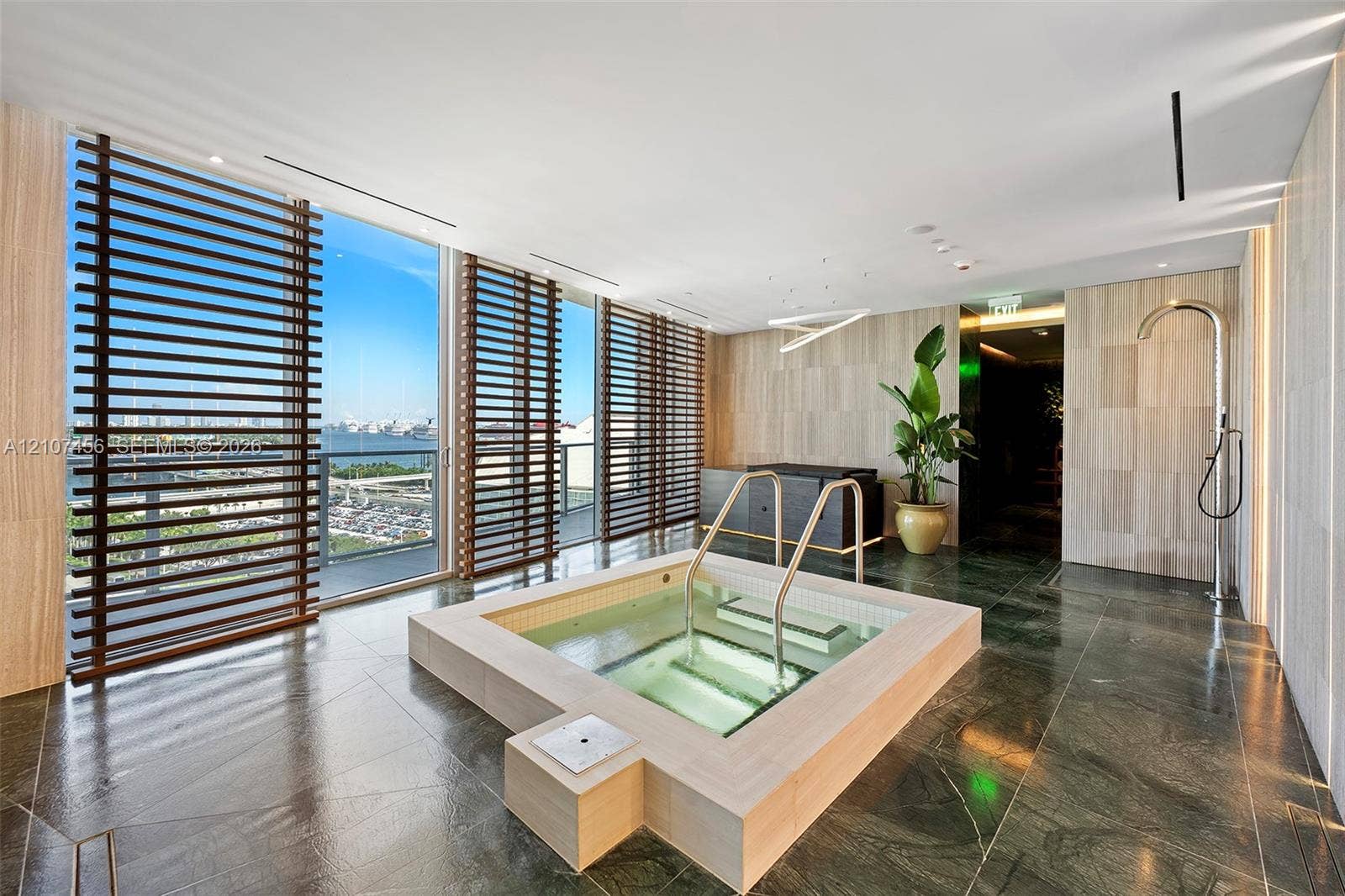 1400 Biscayne Boulevard, #2604, Miami, Miami, FL 33132 Spa room featuring a built-in jetted tub with stone surround, full-height windows with wood-slat privacy screens, polished stone floor tiling, and a wall-mounted rainfall shower head