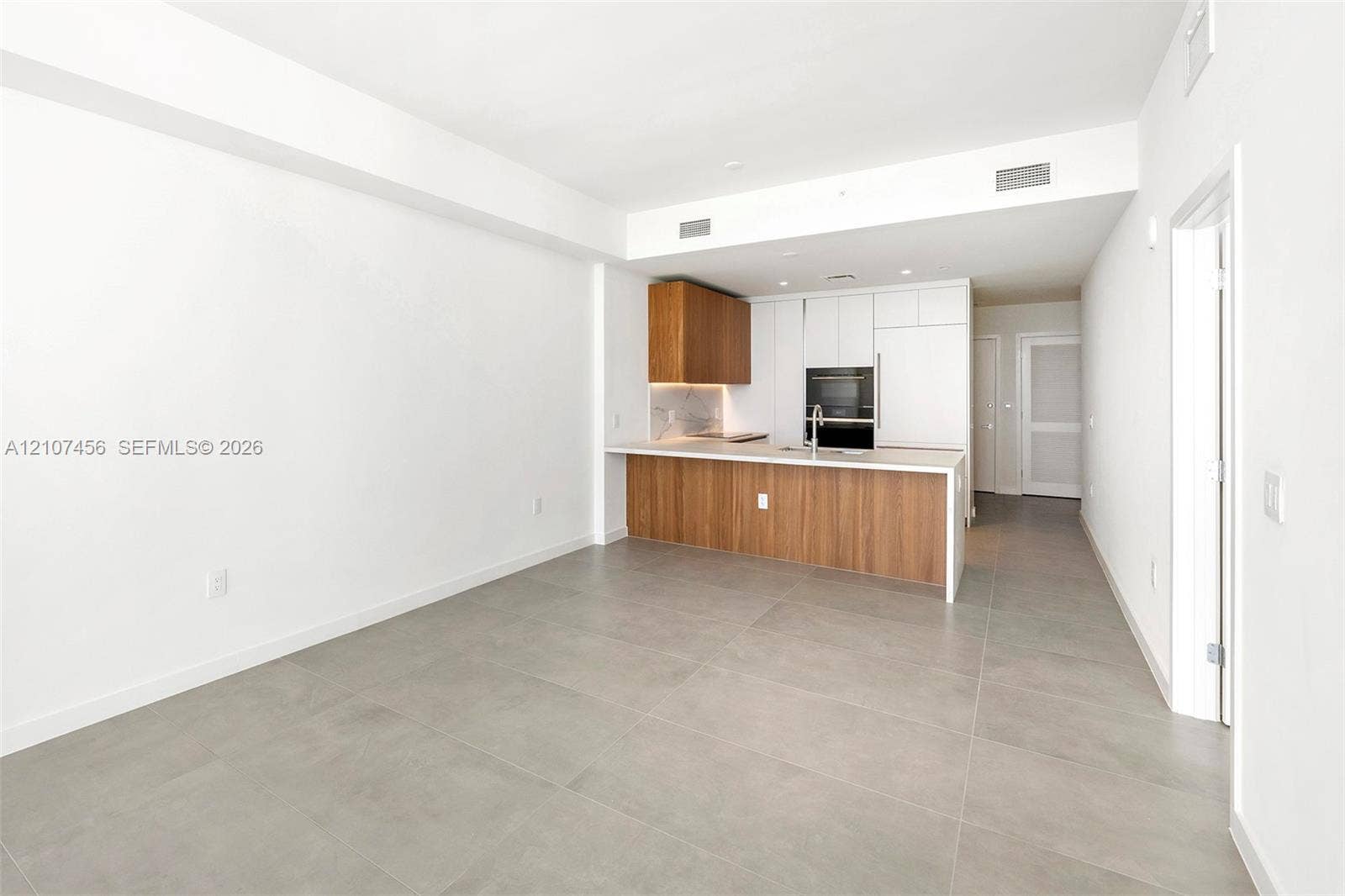 1400 Biscayne Boulevard, #2604, Miami, Miami, FL 33132 Kitchen featuring wood-finish lower cabinetry, white upper cabinets, stone-surfaced countertops, a stainless steel undermount sink, and large-format tile flooring