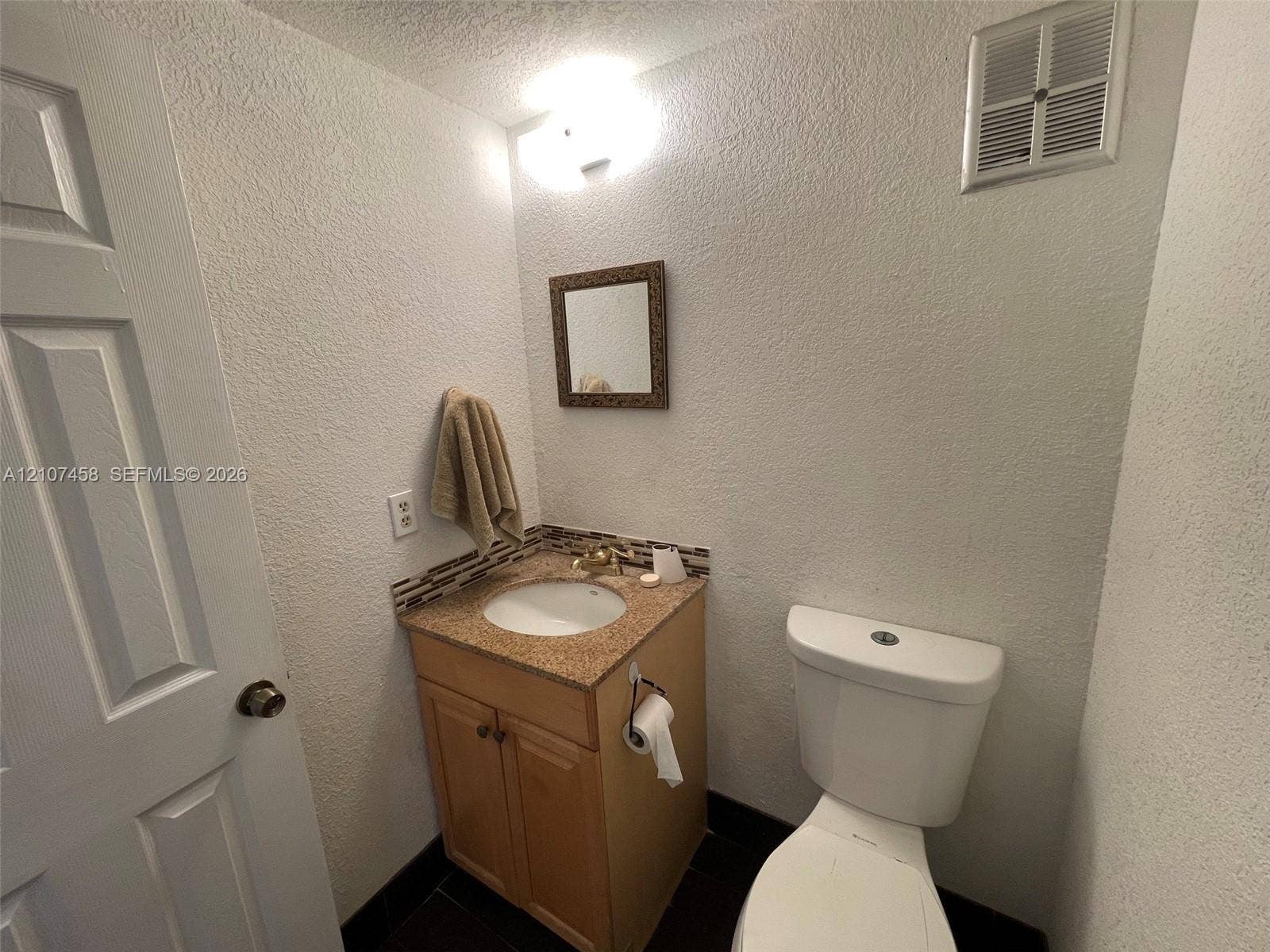 7300 NW 17th Street, #421, Plantation, Plantation, FL 33313 Bathroom featuring a stone-composite countertop, undermount sink, multi-tonal tile backsplash, wood-finish vanity cabinetry, and a wall-mounted vanity mirror