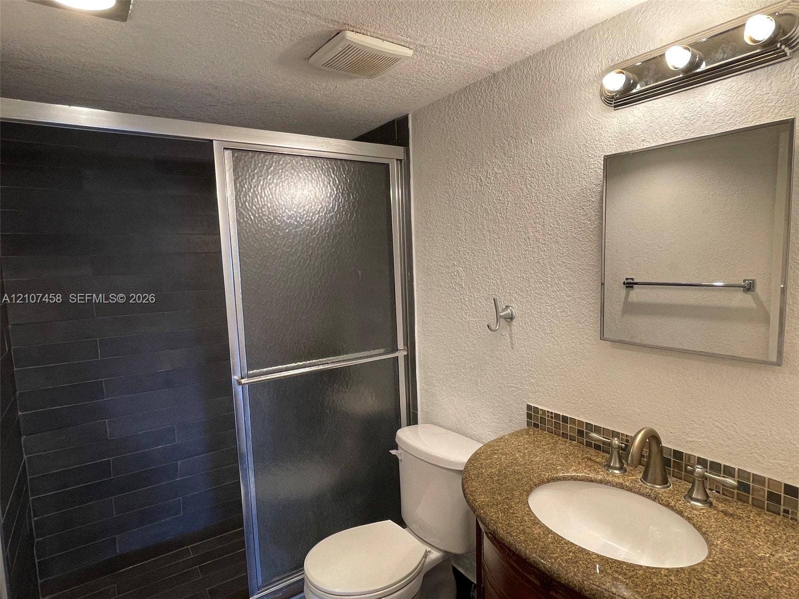 7300 NW 17th Street, #421, Plantation, Plantation, FL 33313 Bathroom featuring a shower stall with dark horizontal tile surround, glass sliding doors, vanity with a curved countertop, integrated oval sink, and mosaic tile backsplash