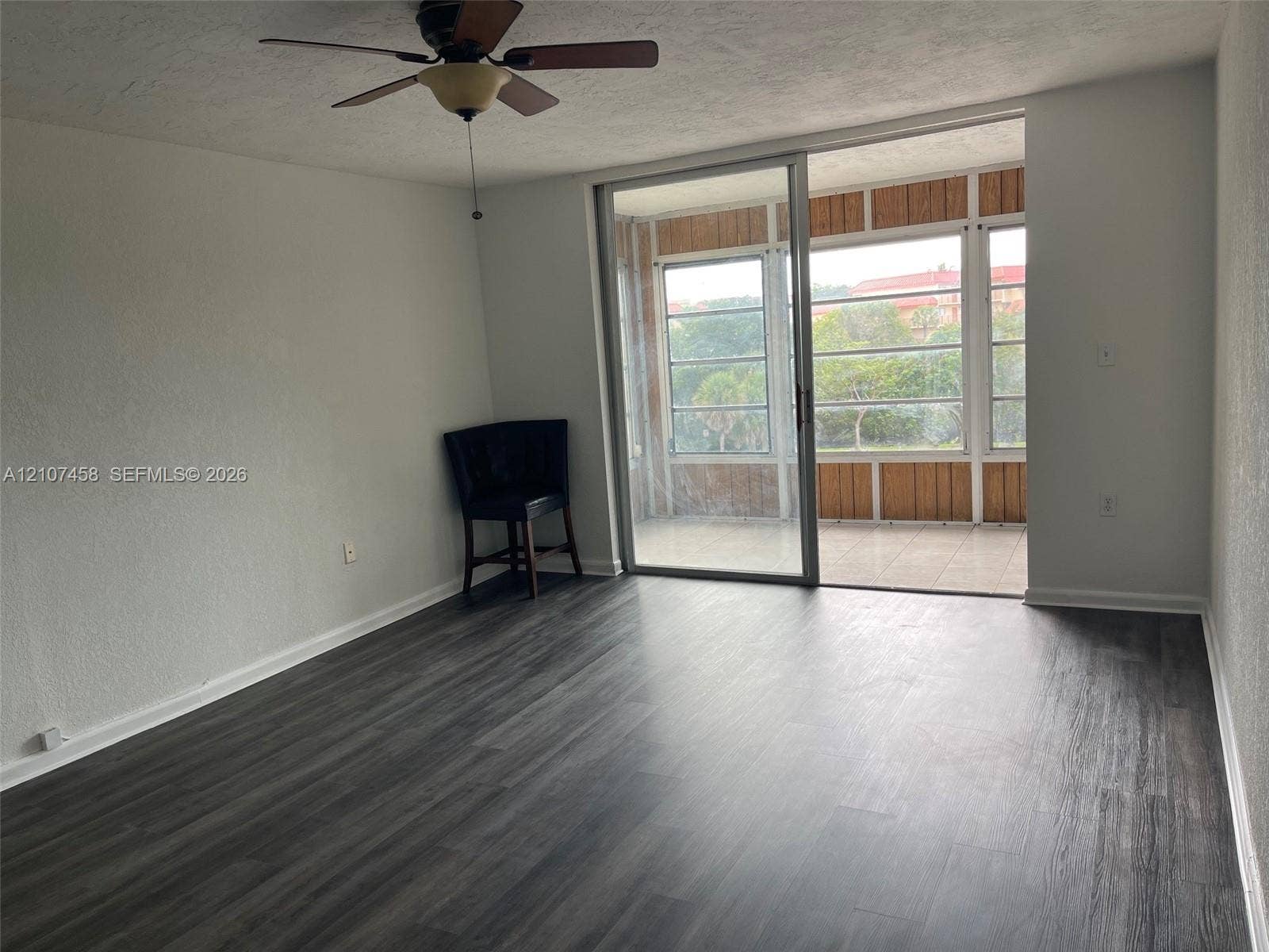 7300 NW 17th Street, #421, Plantation, Plantation, FL 33313 Living area featuring wood-finish flooring, a ceiling fan with integrated lighting, and glass sliding doors opening to a screened-in enclosure with tile flooring and wood-paneled walls