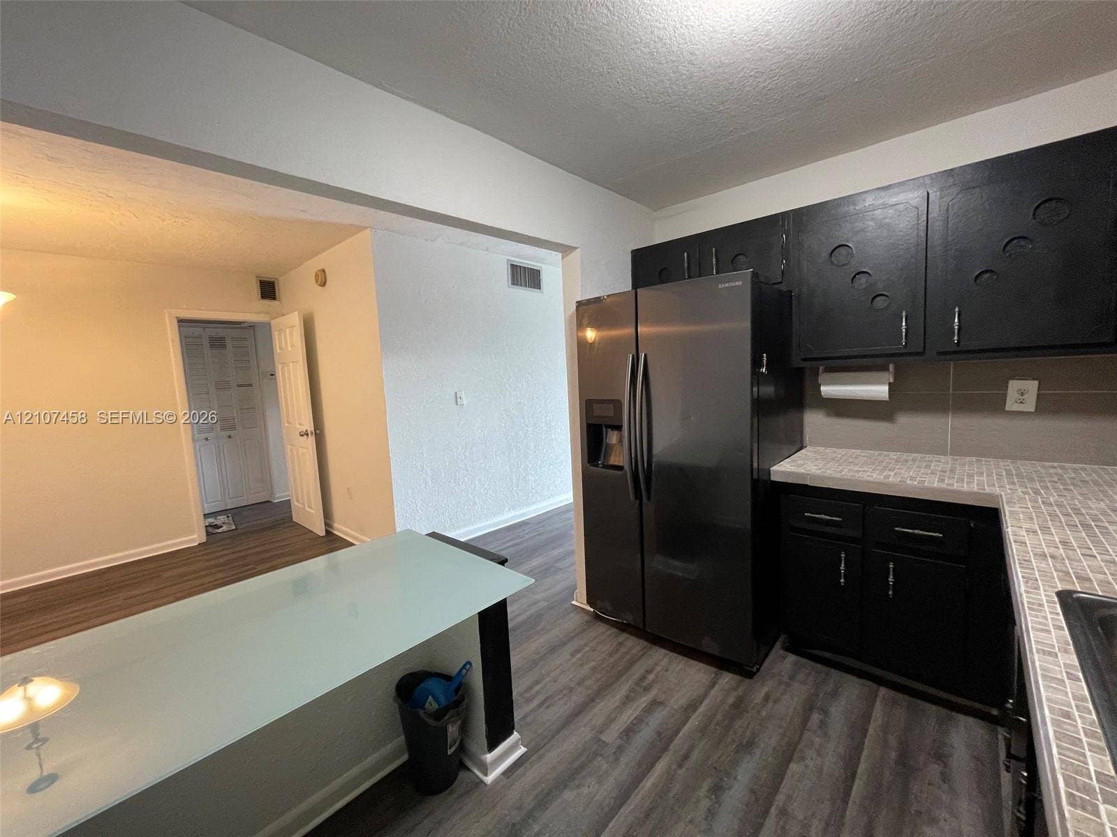 7300 NW 17th Street, #421, Plantation, Plantation, FL 33313 Kitchen featuring dark cabinetry, mosaic tile backsplash, wood-finish flooring, and a frosted glass-top peninsula