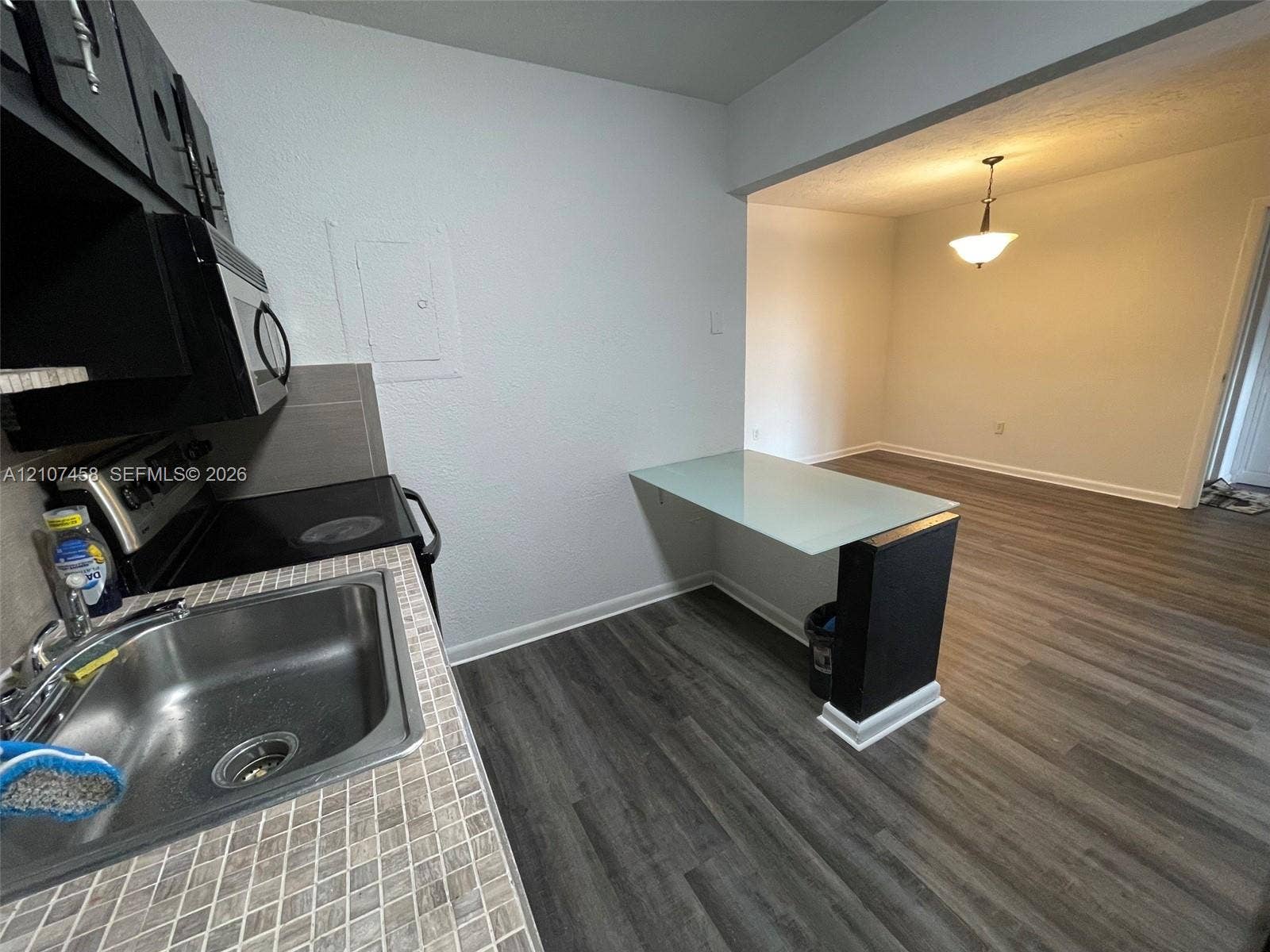 7300 NW 17th Street, #421, Plantation, Plantation, FL 33313 Kitchen featuring a stainless steel drop-in sink, mosaic tile countertops, black cabinetry, wood-finish flooring, and a built-in glass-top breakfast bar