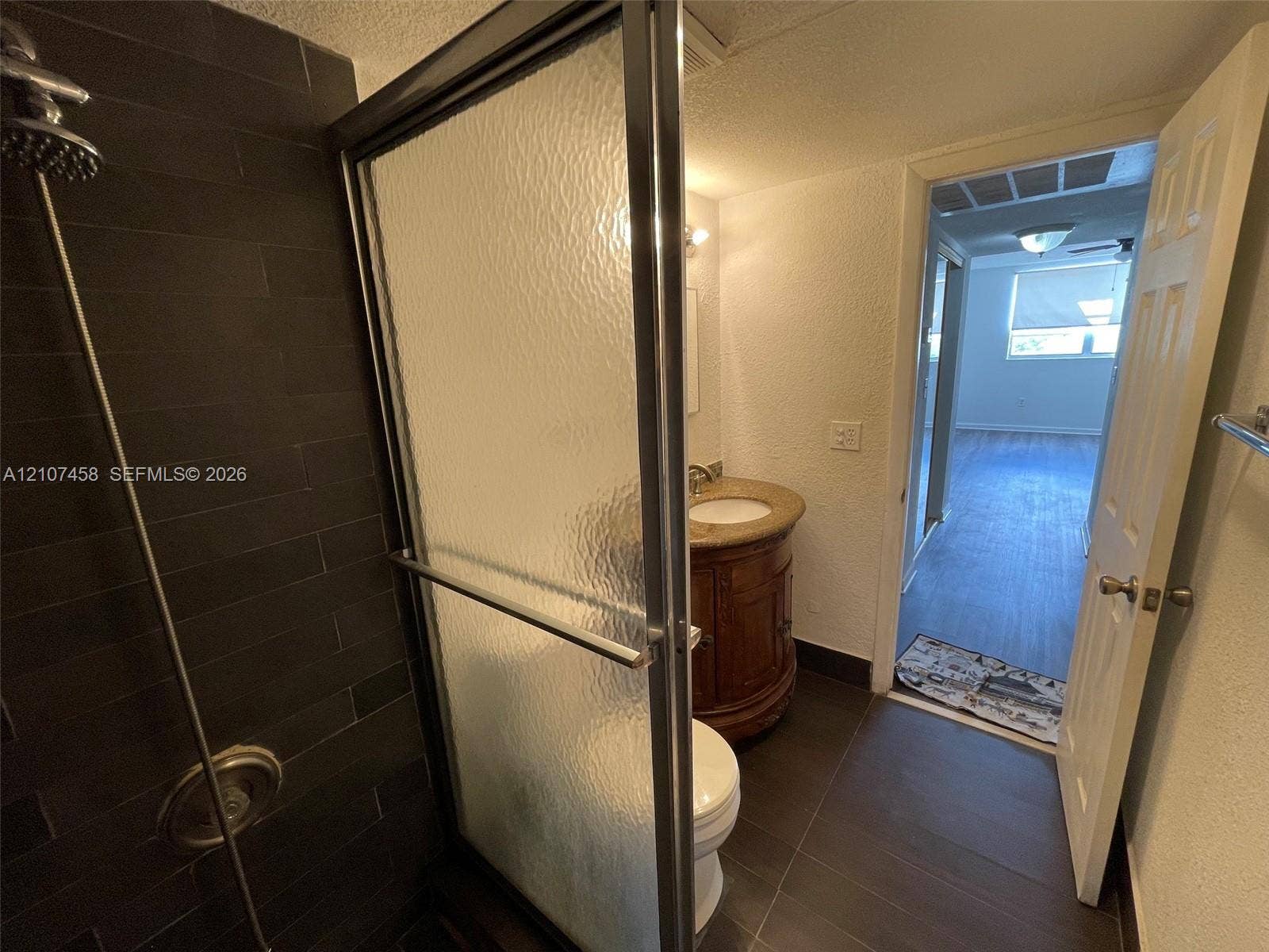7300 NW 17th Street, #421, Plantation, Plantation, FL 33313 Bathroom featuring a glass-enclosed shower with dark rectangular tile surround, wood-finish vanity with a stone countertop, and large-format floor tile