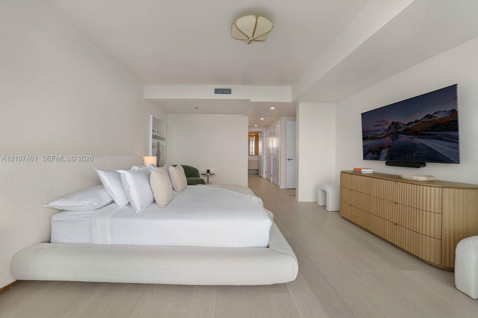 Spacious room featuring light-toned wood-finish flooring, recessed ceiling lighting, a sculpted semi-flush mount fixture, and smooth wall finishes