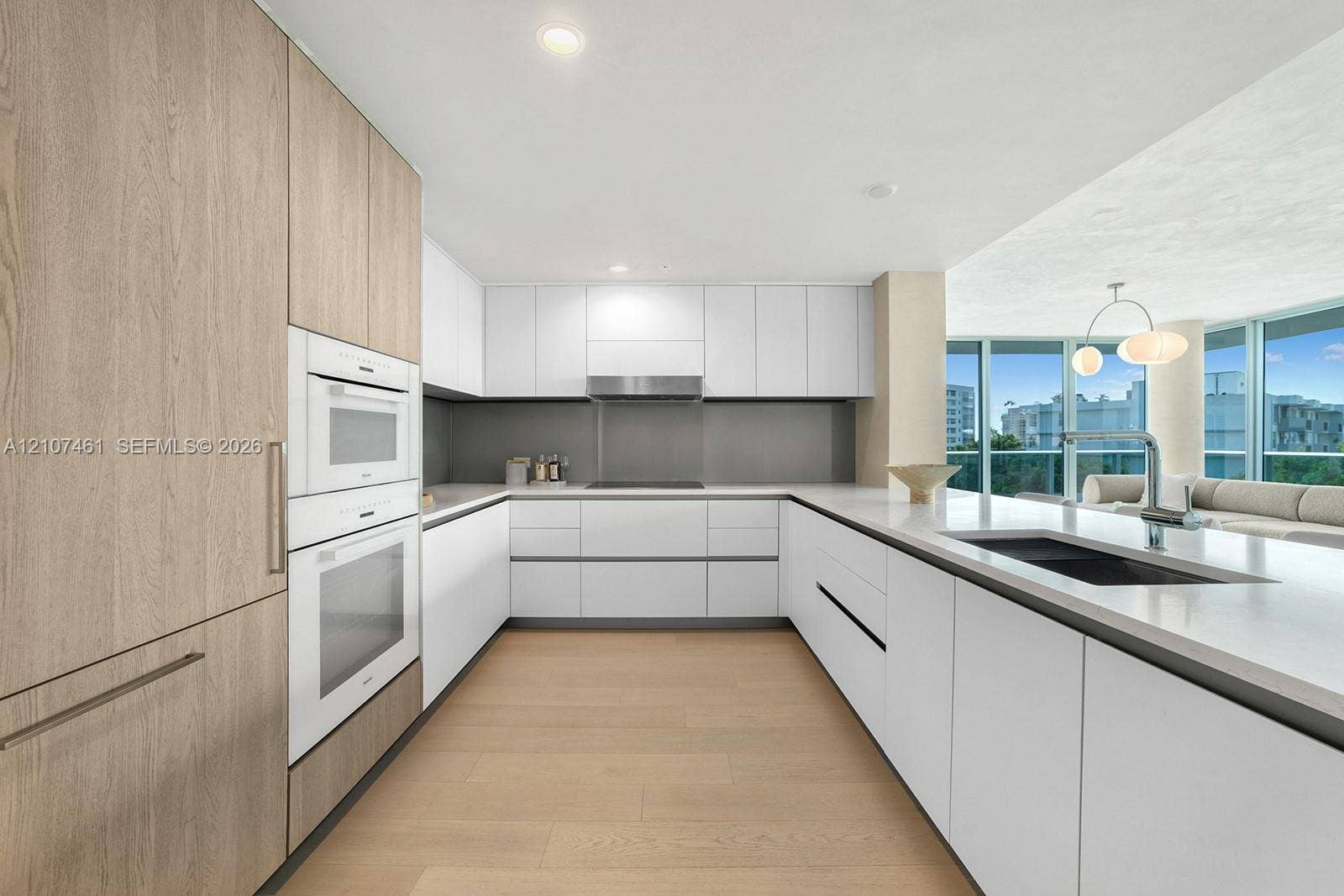 Modern kitchen featuring flat-panel cabinetry, light-toned wood-finish flooring, integrated wall ovens, solid-surface countertops, and recessed lighting