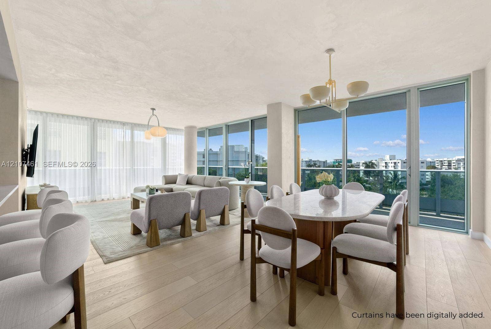 9201 E Bay Harbor Drive, #602, Bal Harbour, FL 33141 Open-concept area featuring light-toned wood-finish flooring, floor-to-ceiling glass paneling, metal-framed terrace access, and dual pendant chandeliers