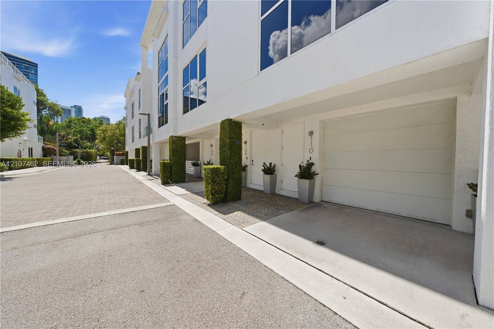 455 NE 39th Street, #110, Miami, FL 33137 Contemporary multi-story exterior featuring a smooth white stucco finish, floor-to-ceiling windows, integrated garage door, and manicured topiary accents