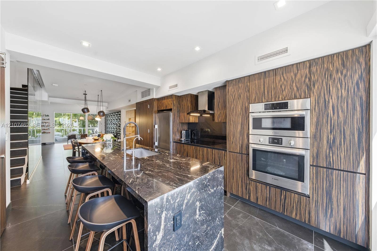 455 NE 39th Street, #110, Miami, FL 33137 Kitchen featuring wood-finish flat-panel cabinetry, stone-surfaced waterfall island, stainless steel wall-mounted oven and microwave, and large-format tile flooring