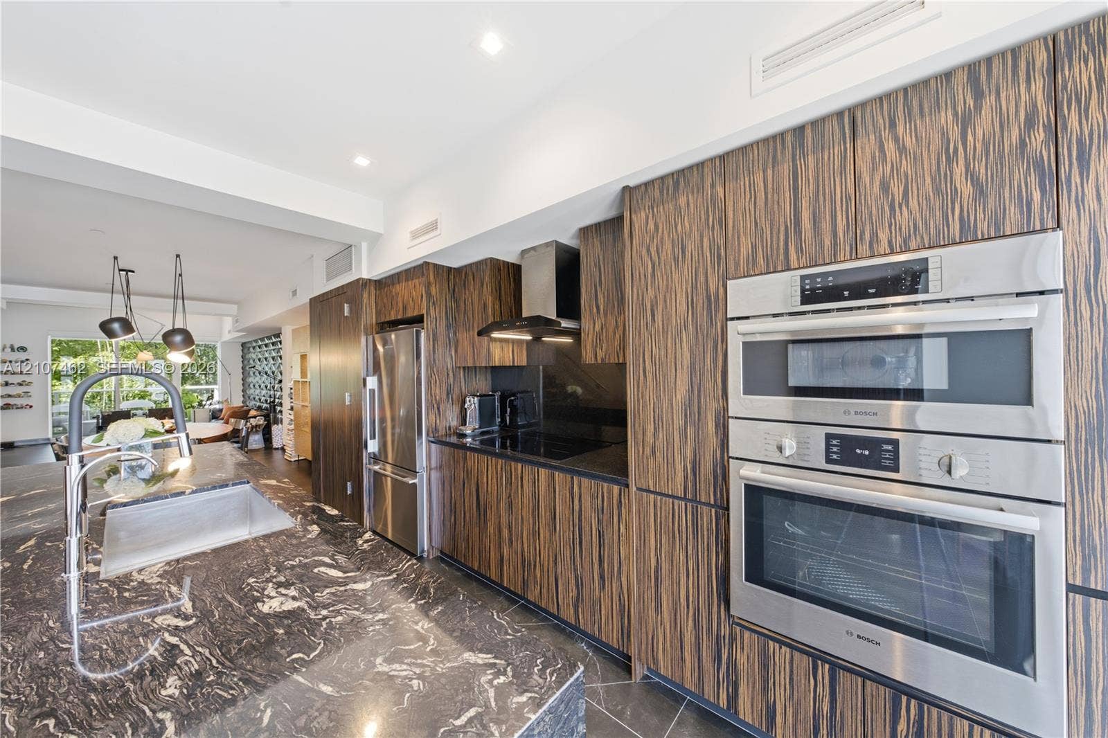 455 NE 39th Street, #110, Miami, FL 33137 Kitchen featuring horizontal-grain wood cabinetry, integrated stainless steel appliances, dark stone countertops, stone flooring, and recessed ceiling lighting