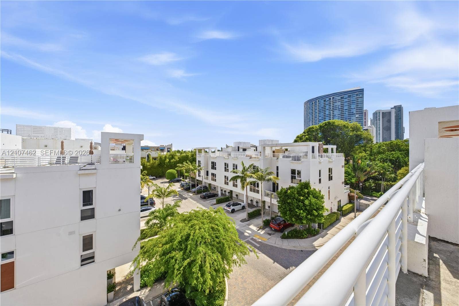455 NE 39th Street, #110, Miami, FL 33137 Elevated outdoor balcony with white railings overlooking a residential complex featuring multi-level structures, paved driveways, and mature landscaping