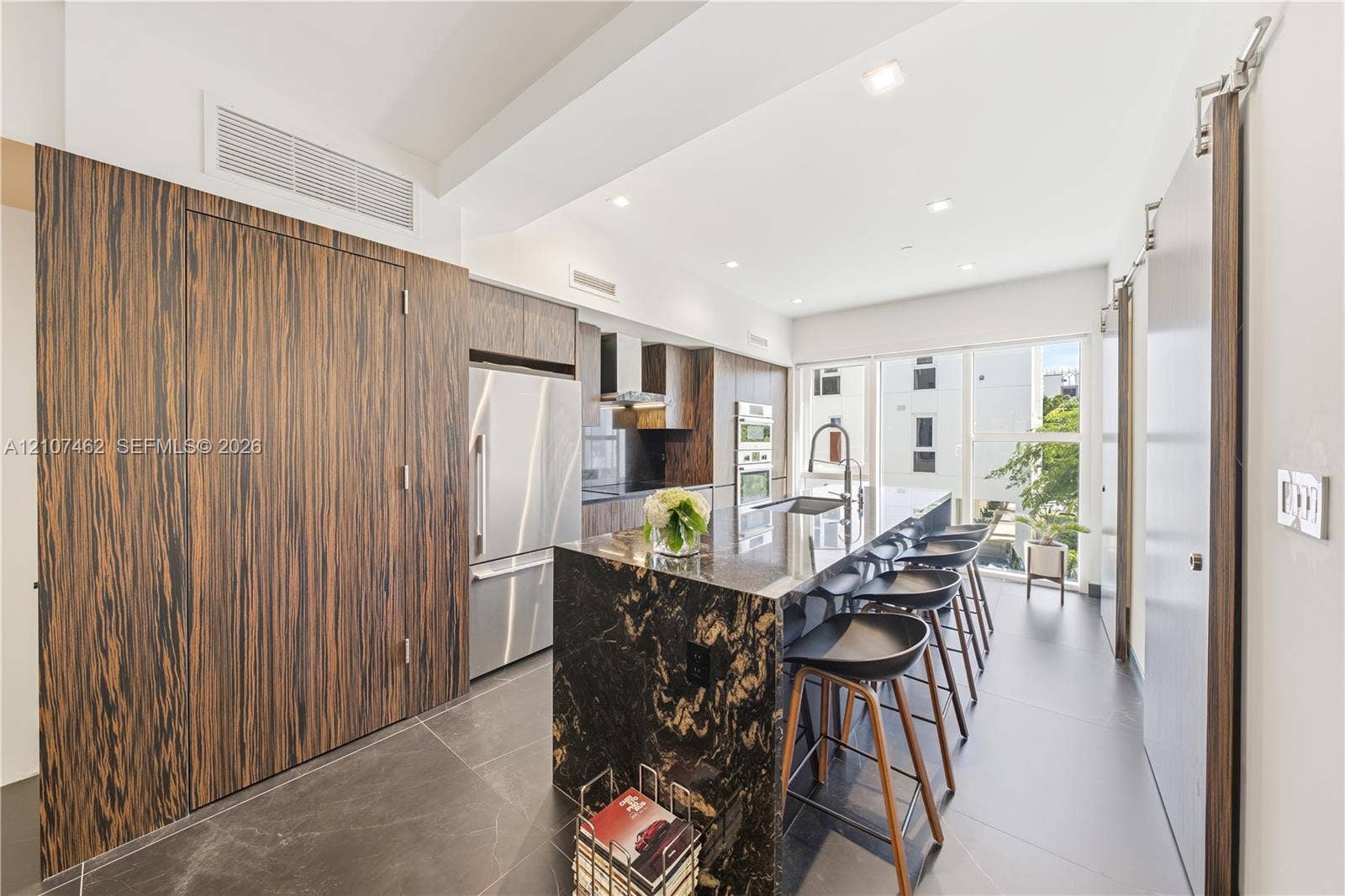 455 NE 39th Street, #110, Miami, FL 33137 Kitchen featuring full-height wood-finish cabinetry, a waterfall-edge stone island, built-in stainless steel appliances, large-format tile flooring, and recessed ceiling lighting