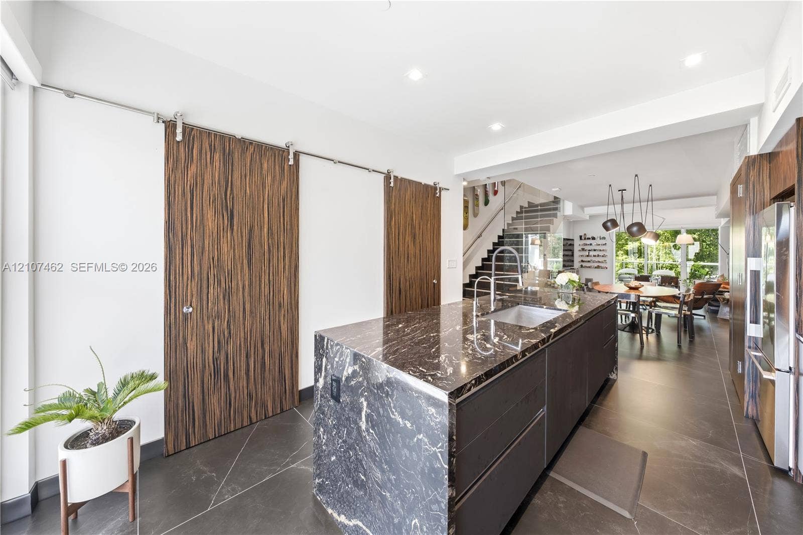 455 NE 39th Street, #110, Miami, FL 33137 Kitchen island with dark stone waterfall countertop and integrated sink, flat-panel cabinetry, wood-finish sliding barn doors, and large-format tile flooring