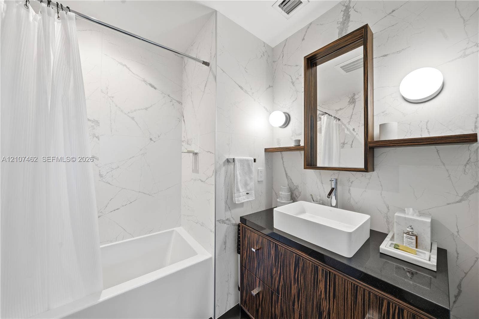 455 NE 39th Street, #110, Miami, FL 33137 Bathroom featuring large-format wall tiling, a dark stone vanity countertop, a rectangular vessel sink, a wood-finish vanity cabinet, and wall-mounted vanity lighting
