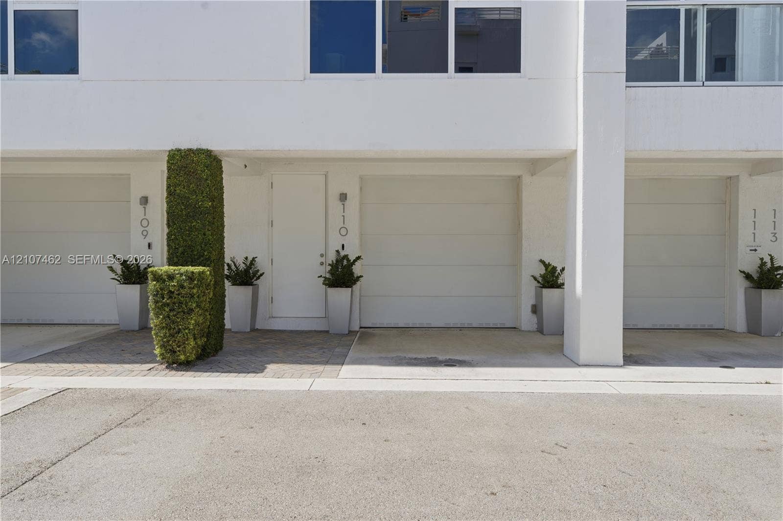 455 NE 39th Street, #110, Miami, FL 33137 Modern exterior facade featuring crisp white stucco finishes, horizontal panel garage doors, concrete driveway, and paver entryway
