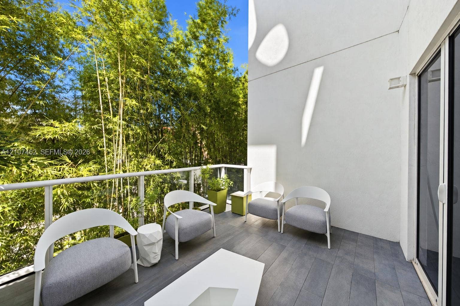 455 NE 39th Street, #110, Miami, FL 33137 Private balcony featuring gray wood-finish decking, a white metal railing with glass panels, and mature bamboo landscaping