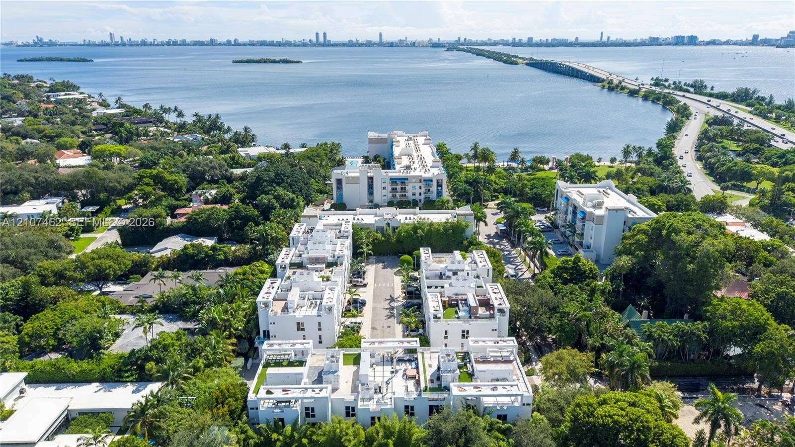 455 NE 39th Street, #110, Miami, FL 33137 Aerial perspective of a multi-structure residential complex featuring white stucco facades, flat roofs, private rooftop terraces, and mature perimeter landscaping, situated along a coastal waterfront
