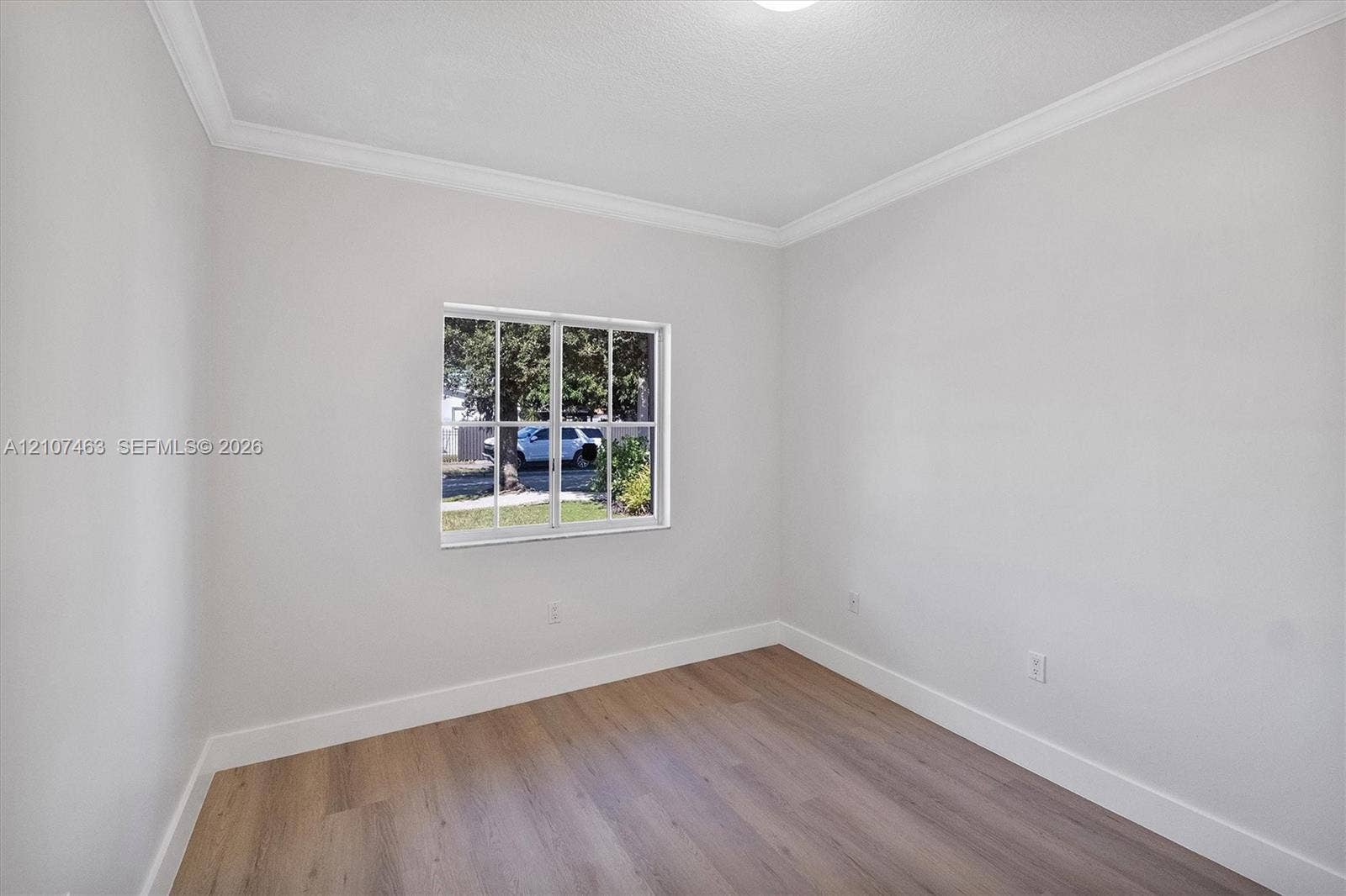 7071 W 6th Avenue, #N/A, Hialeah, Hialeah, FL 33014 Room 2 Neutral-toned interior space featuring wood-finish flooring, white walls, crown molding, and a grid-pane window