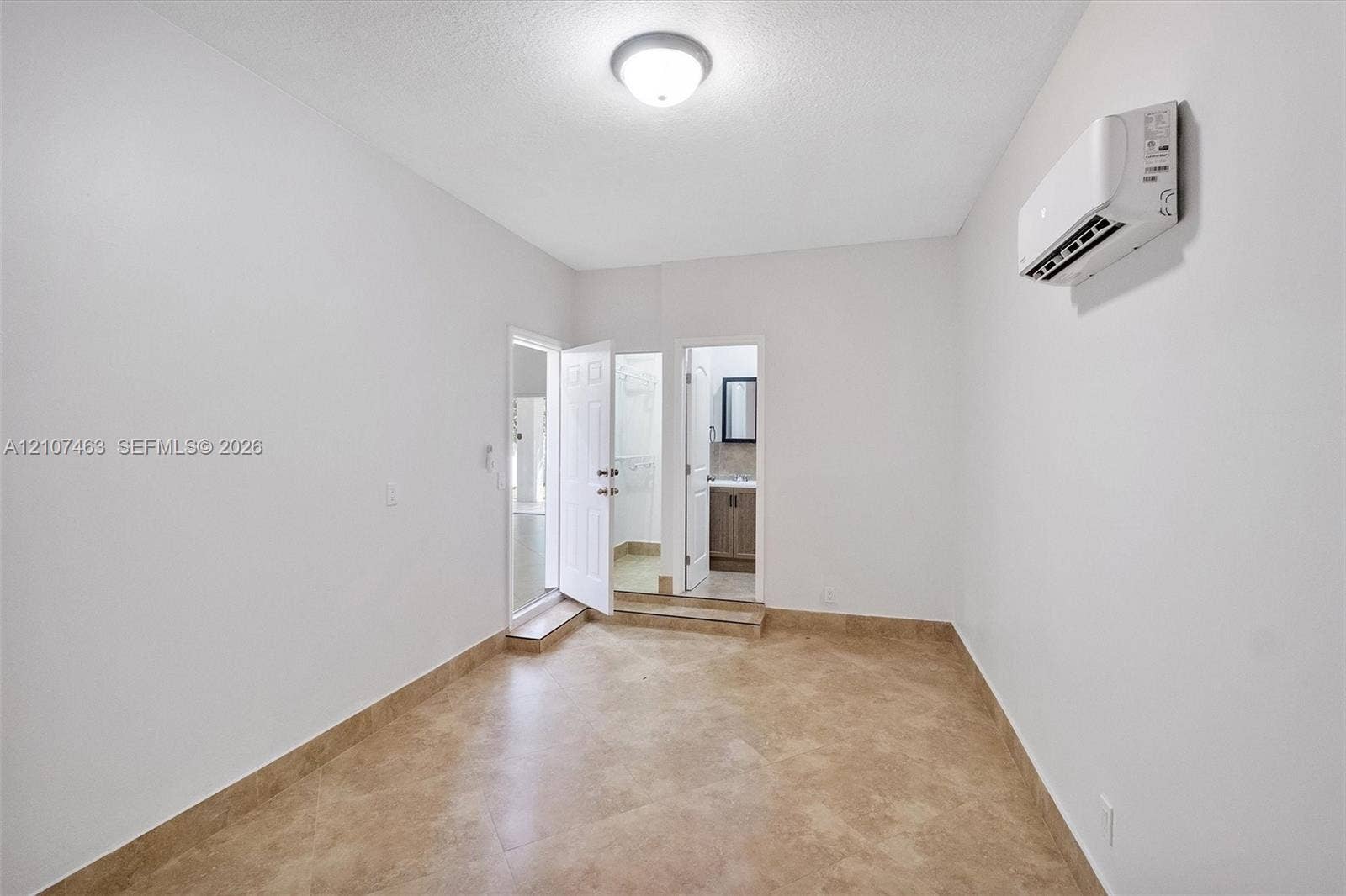 7071 W 6th Avenue, #N/A, Hialeah, Hialeah, FL 33014 Interior room 3 featuring neutral-toned tile flooring, white wall finishes, a wall-mounted ductless climate control unit, and a flush-mount ceiling light fixture