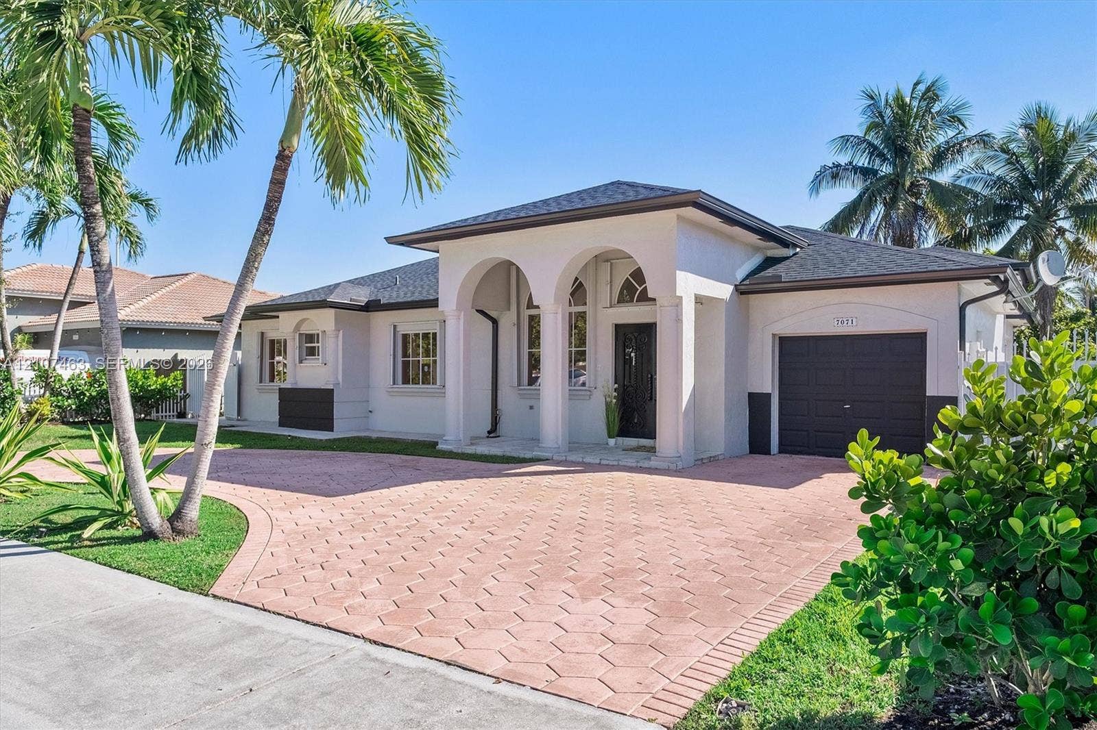 7071 W 6th Avenue, #N/A, Hialeah, Hialeah, FL 33014 Single-story exterior featuring a covered arched entryway, hexagonal paved driveway, dark-toned garage door, and mature palm trees
