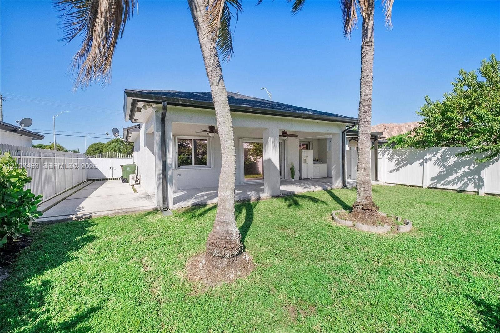 7071 W 6th Avenue, #N/A, Hialeah, Hialeah, FL 33014 Backyard featuring a covered patio, concrete hardscaping, white vinyl privacy fencing, and mature palm trees