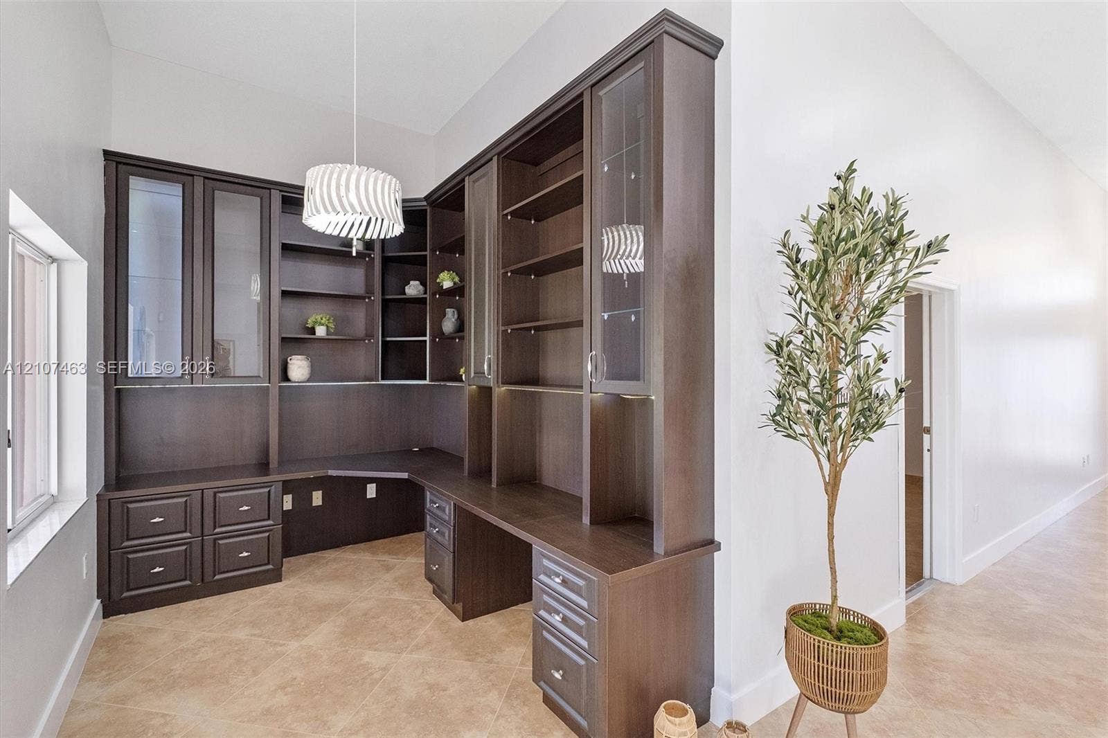 7071 W 6th Avenue, #N/A, Hialeah, Hialeah, FL 33014 Built-in dark wood cabinetry featuring glass-front display doors, open shelving, integrated desk surface, and drawer storage, complemented by high ceilings and neutral tile flooring