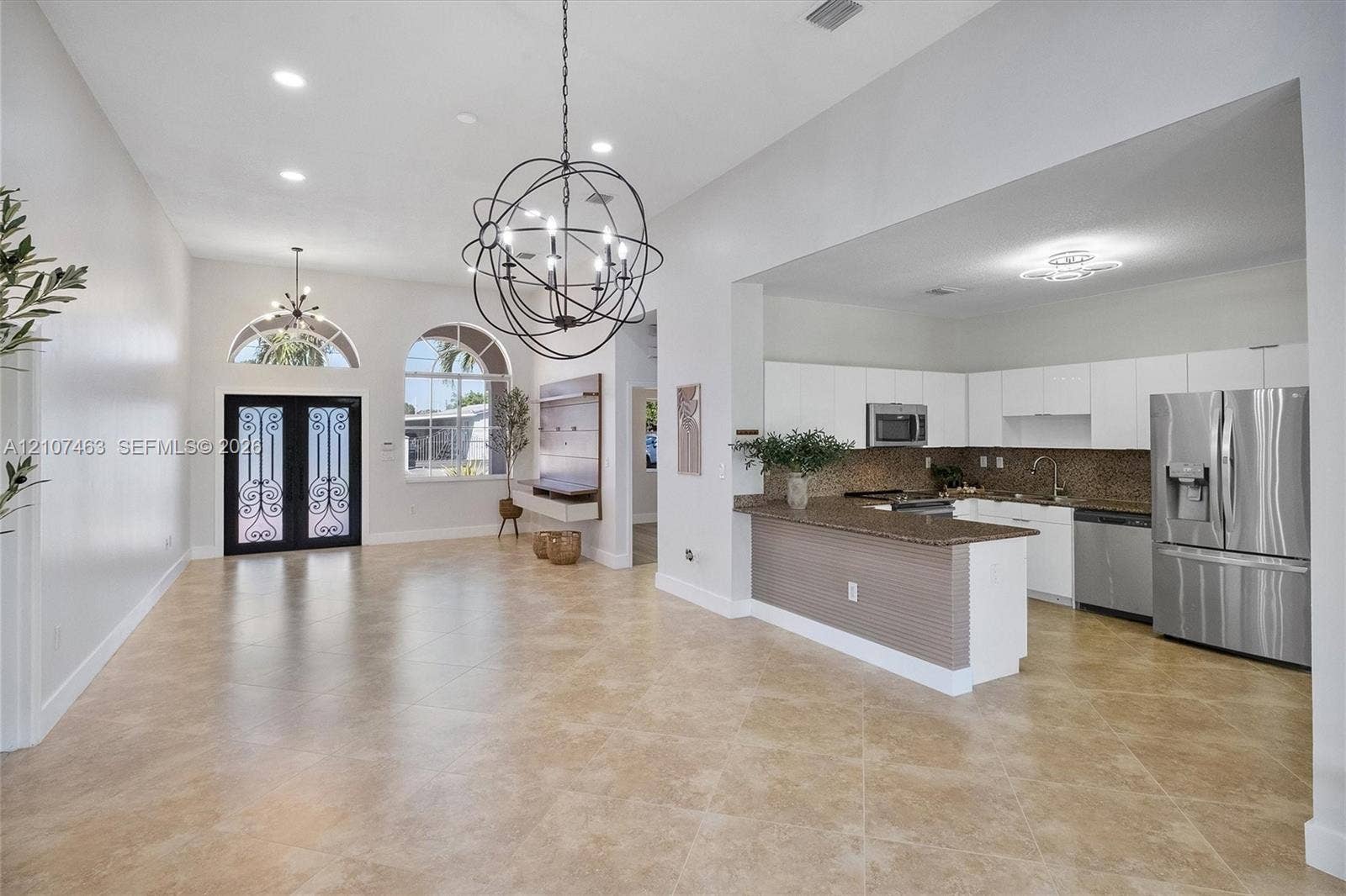 7071 W 6th Avenue, #N/A, Hialeah, Hialeah, FL 33014 Open-concept interior featuring large-format tile flooring, arched windows with decorative double entry doors, a spherical multi-light chandelier, and a kitchen equipped with flat-panel cabinetry and stainless steel appliances