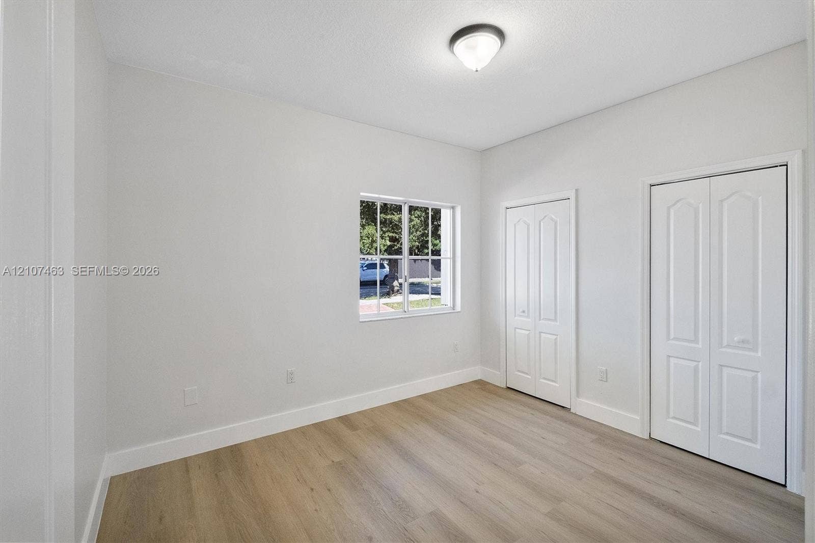 7071 W 6th Avenue, #N/A, Hialeah, Hialeah, FL 33014 Room 1 featuring wood-finish flooring, a multi-pane window, dual closet doors with arched paneling, and a flush-mount light fixture