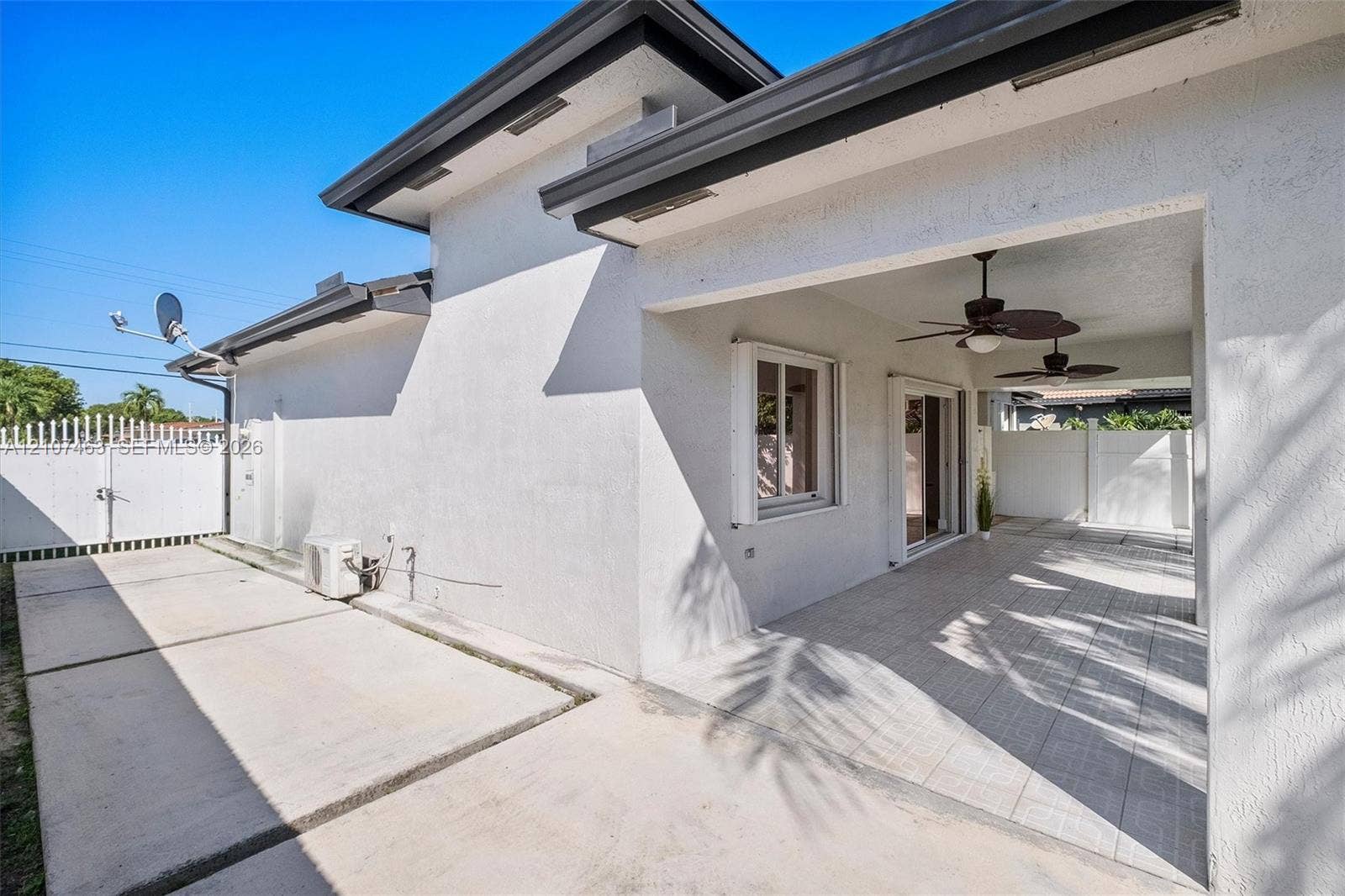 7071 W 6th Avenue, #N/A, Hialeah, Hialeah, FL 33014 Stucco exterior featuring a covered patio with dual ceiling fans, tile flooring, sliding glass doors, and concrete hardscaping