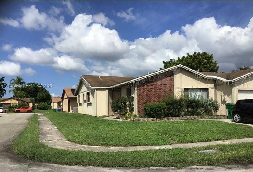 9721 W Daffodil Lane, Miramar, FL 33025 Single-story residence featuring a brick exterior accent, gabled roofline, and an attached garage